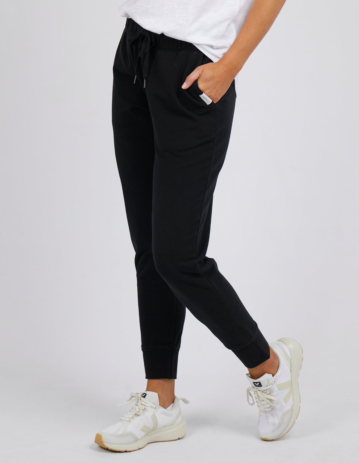 Woman wearing Foxwood black lazy day tracksuit pants with a white singlet on a white background