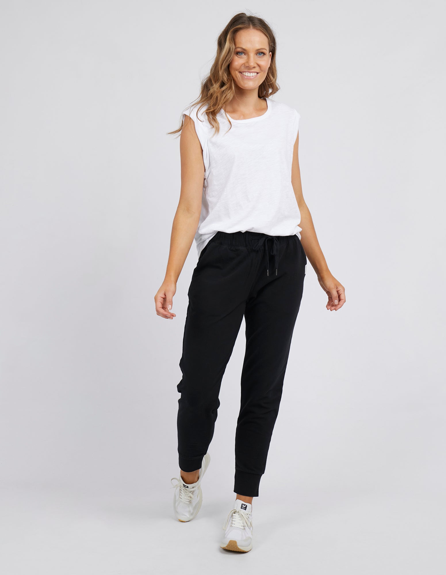 Image of Woman wearing Foxwood black lazy day tracksuit pants with a white singlet on a white background