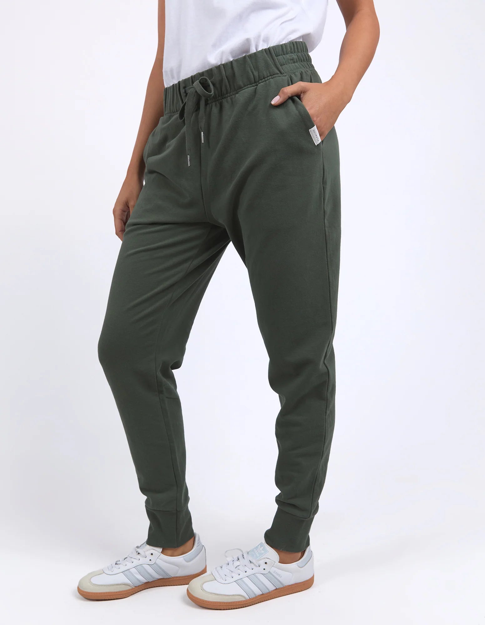 Woman wearing Foxwood green jogger pants and white sneakers on a white background