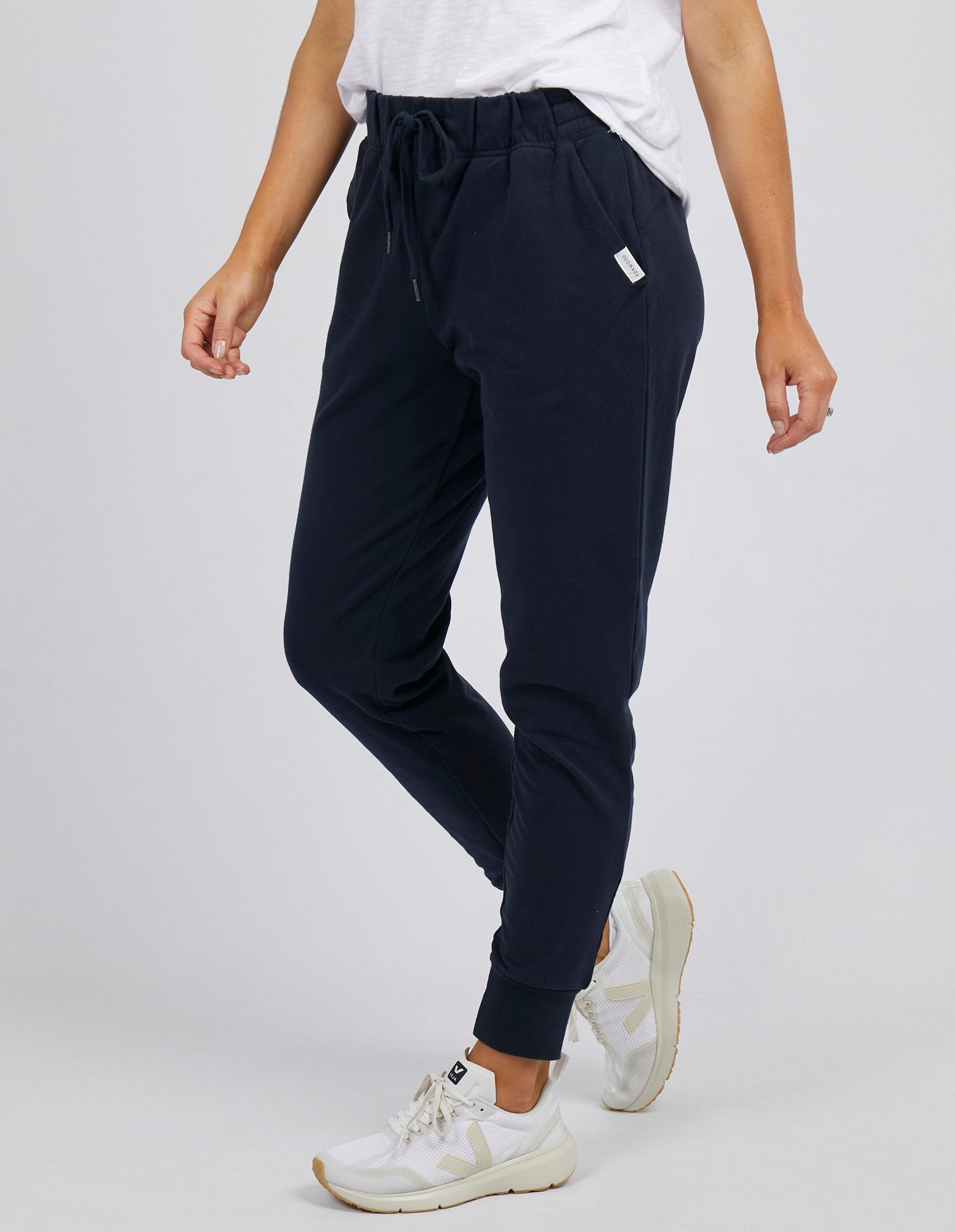 Woman wearing Foxwood lazy day trackpants in navy paired with a white singlet on a white background