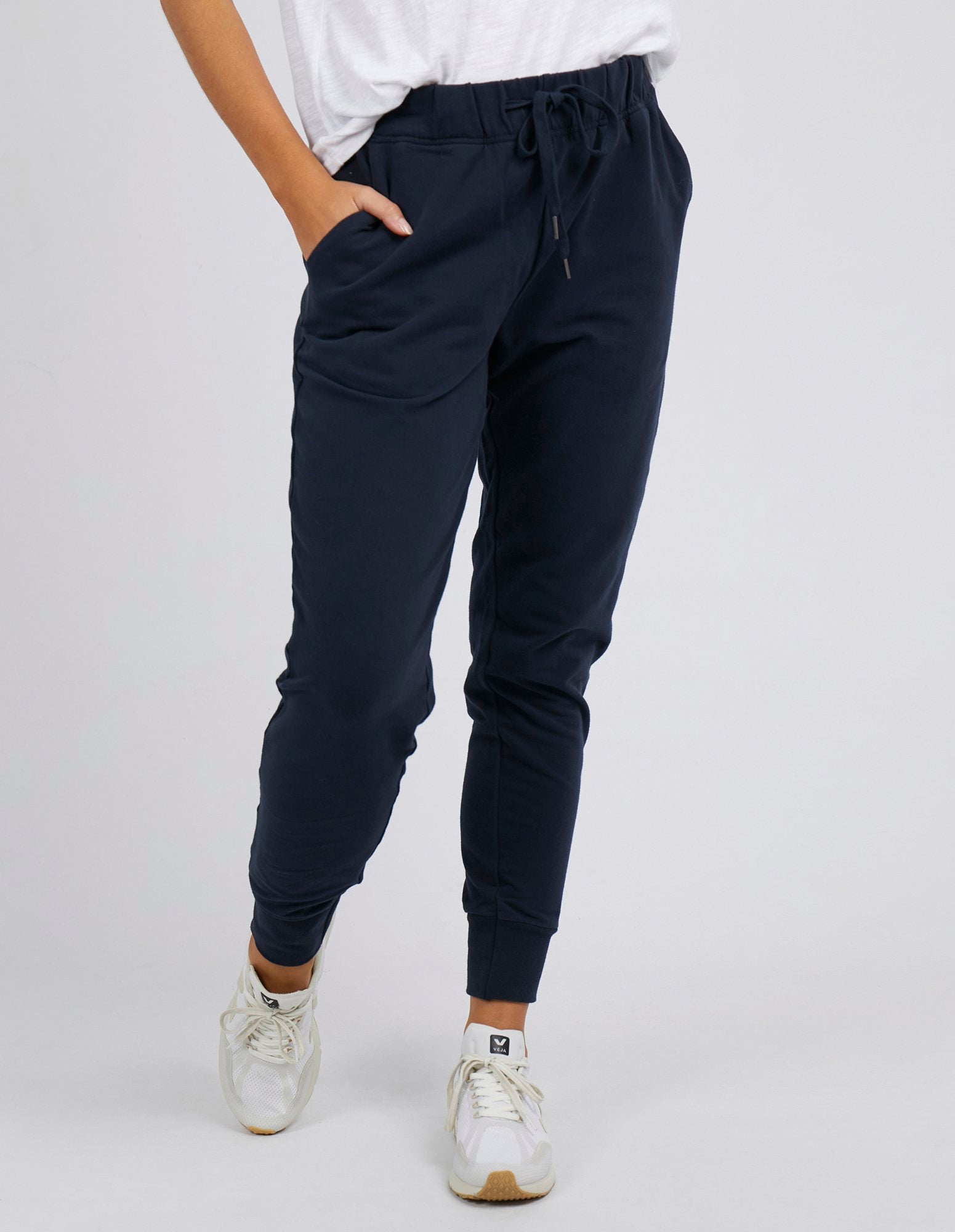 Woman wearing Foxwood lazy day trackpants in navy paired with a white singlet on a white background