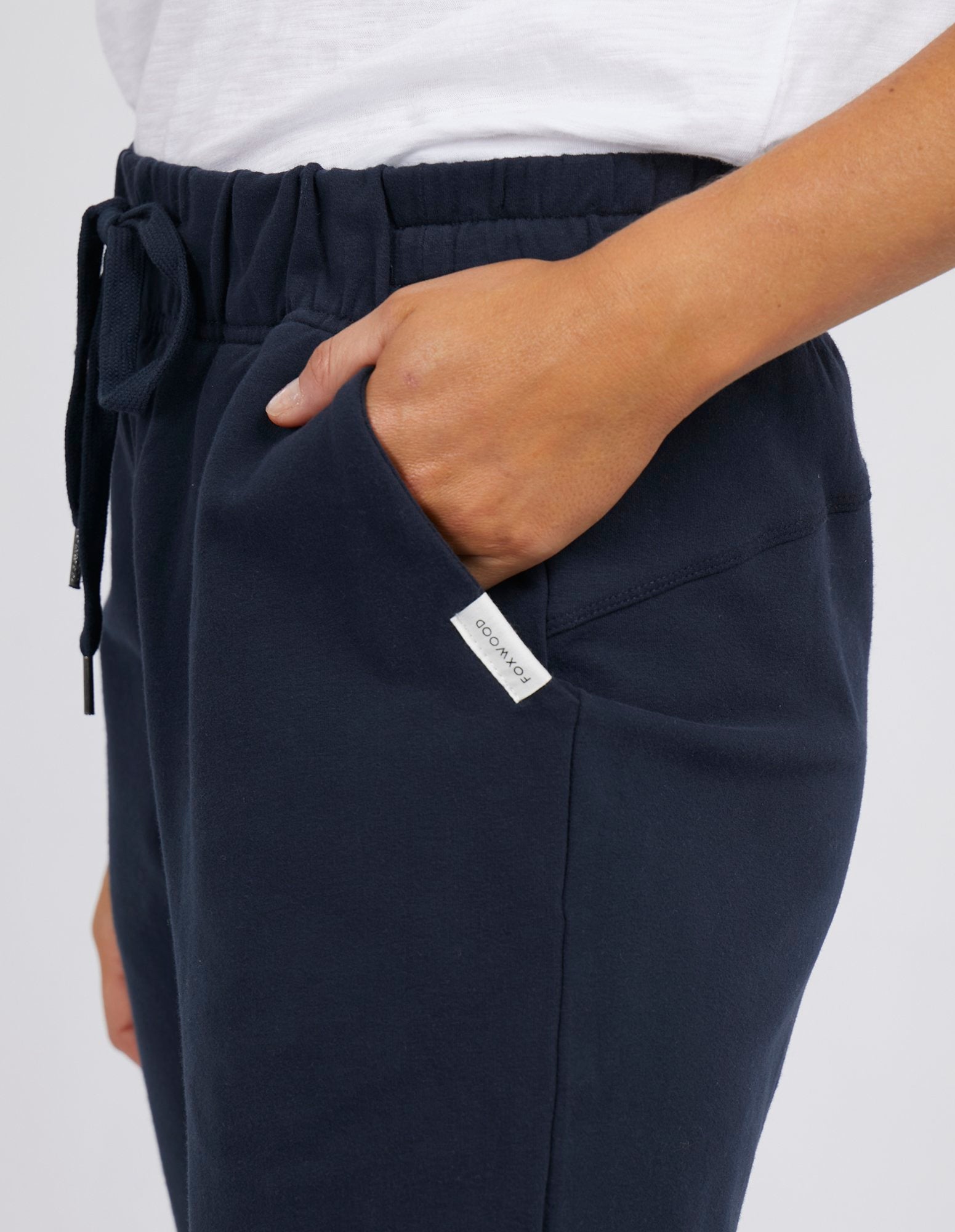 Image of Woman wearing Foxwood lazy day trackpants in navy paired with a white singlet on a white background