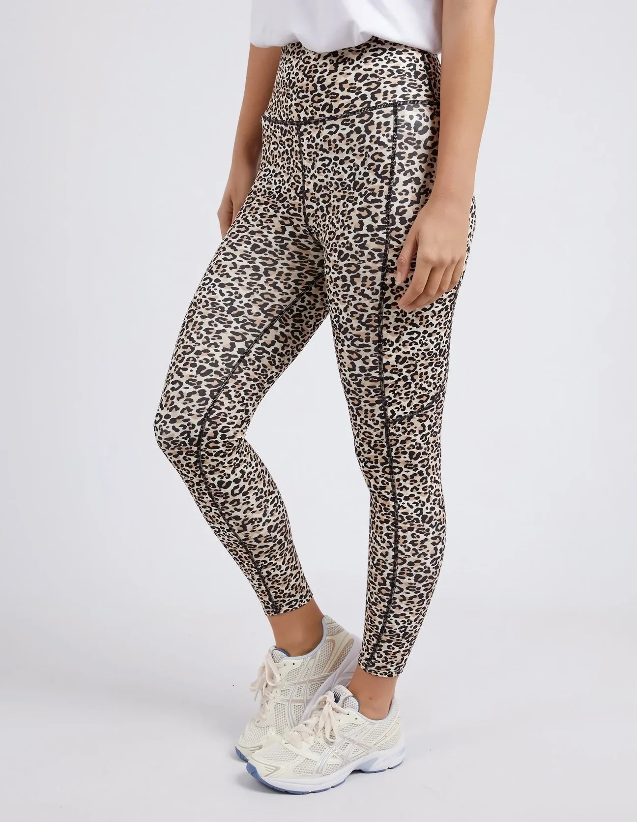 Image of A model wearing high-waisted Foxwood leopard print leggings and white sneakers, cropped from the waist down against a light gray studio background.