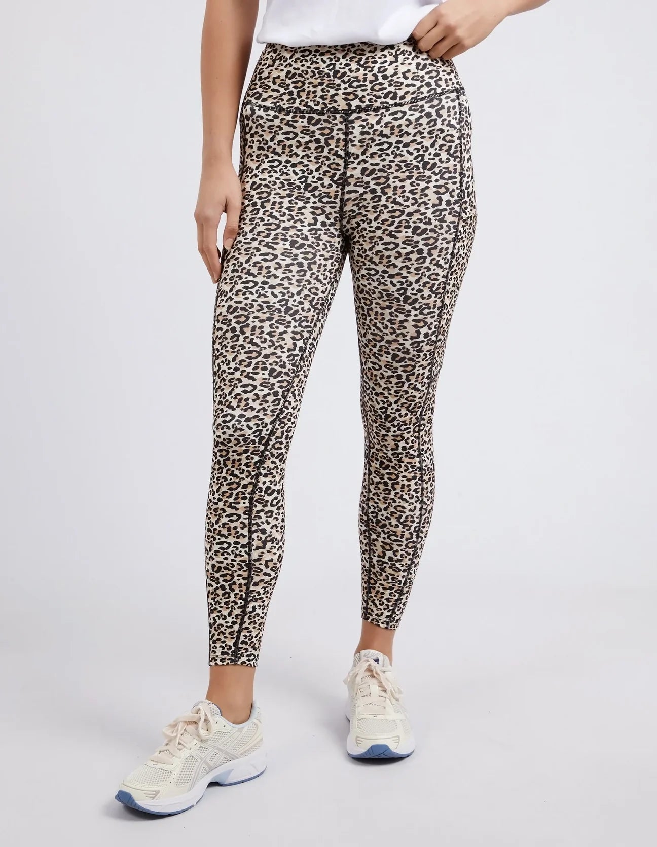 A model wearing high-waisted Foxwood leopard print leggings and white athletic sneakers, shown from the waist down against a light gray studio background.