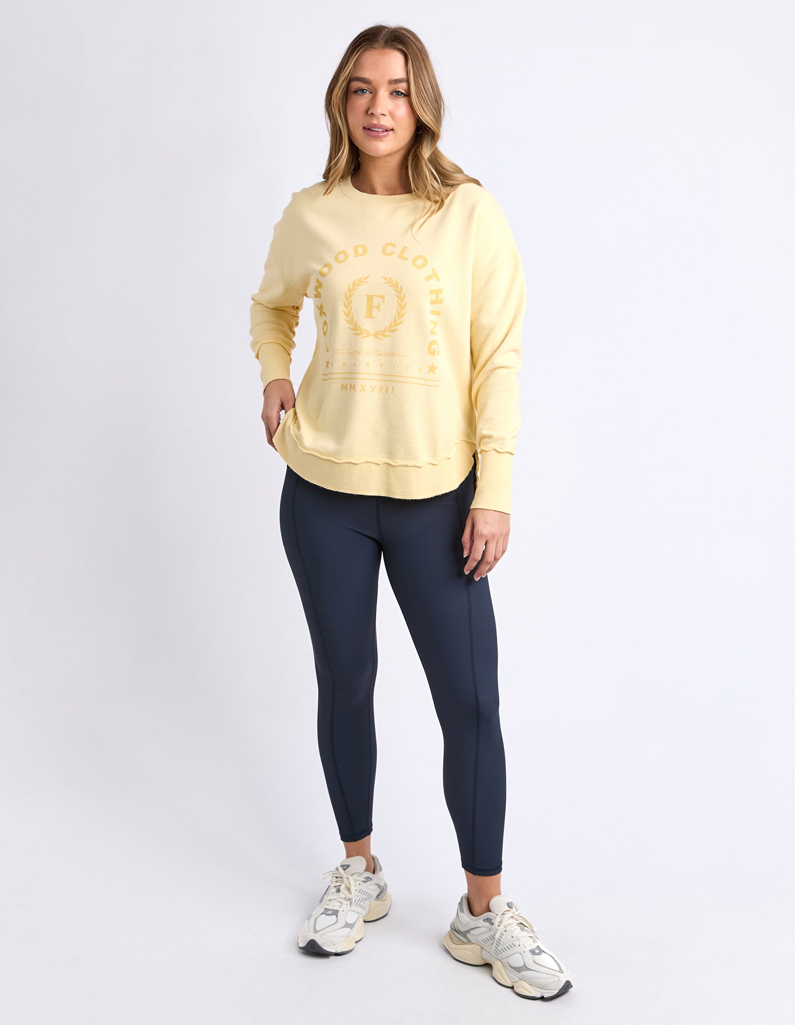 Woman wearing a Foxwood yellow sweatshirt and navy leggings on a white background
