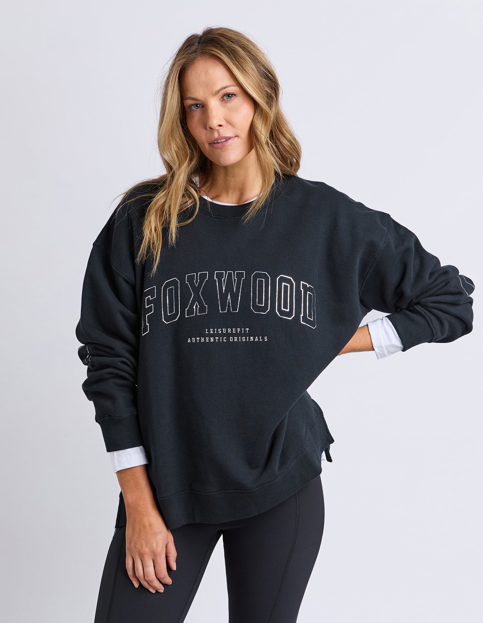 Image of Woman wearing a black 'FOXWOOD' sweatshirt on a light gray background
