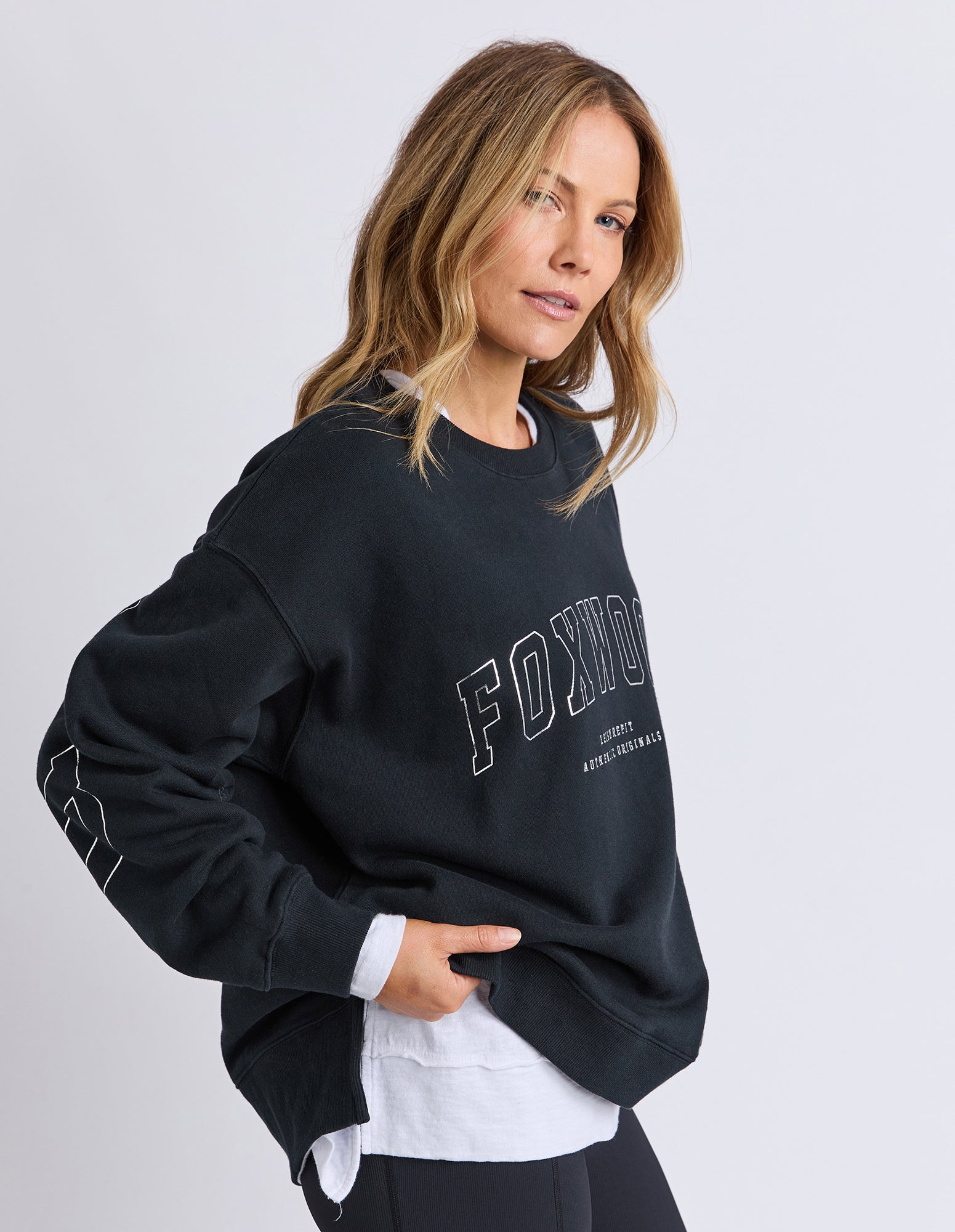 Woman wearing a black sweatshirt with 'FOX' branding on a light gray background