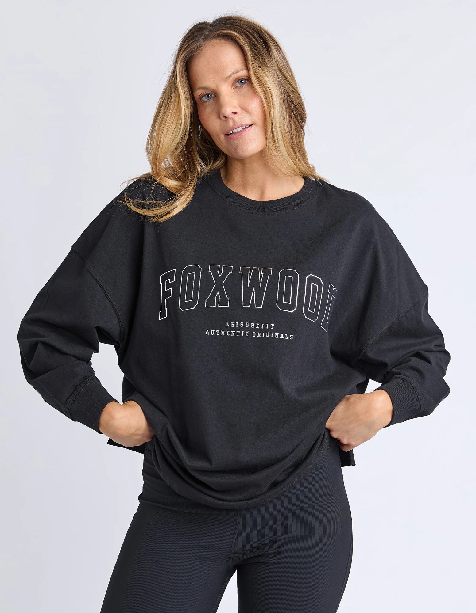 Image of Woman wearing Foxwood long sleeve top with Foxwood branding pictured on the front and back of top. Top paired with black leggings on a plain background