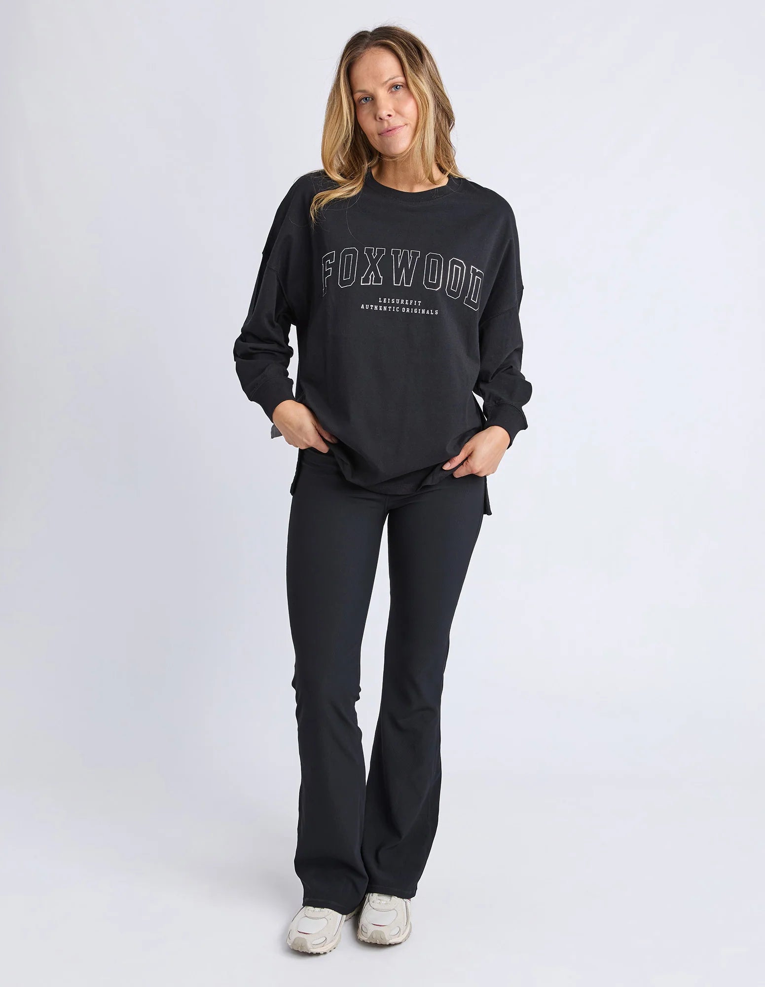 Woman wearing Foxwood long sleeve top with Foxwood branding pictured on the front and back of top. Top paired with black leggings on a plain background