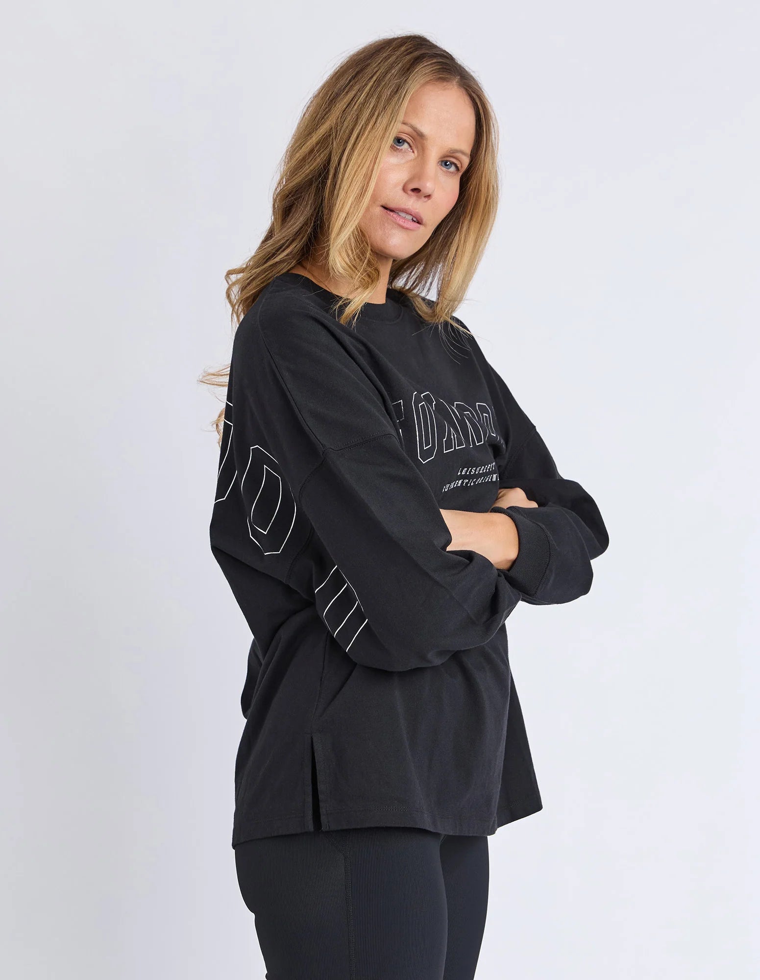 Image of Woman wearing Foxwood long sleeve top with Foxwood branding pictured on the front and back of top. Top paired with black leggings on a plain background