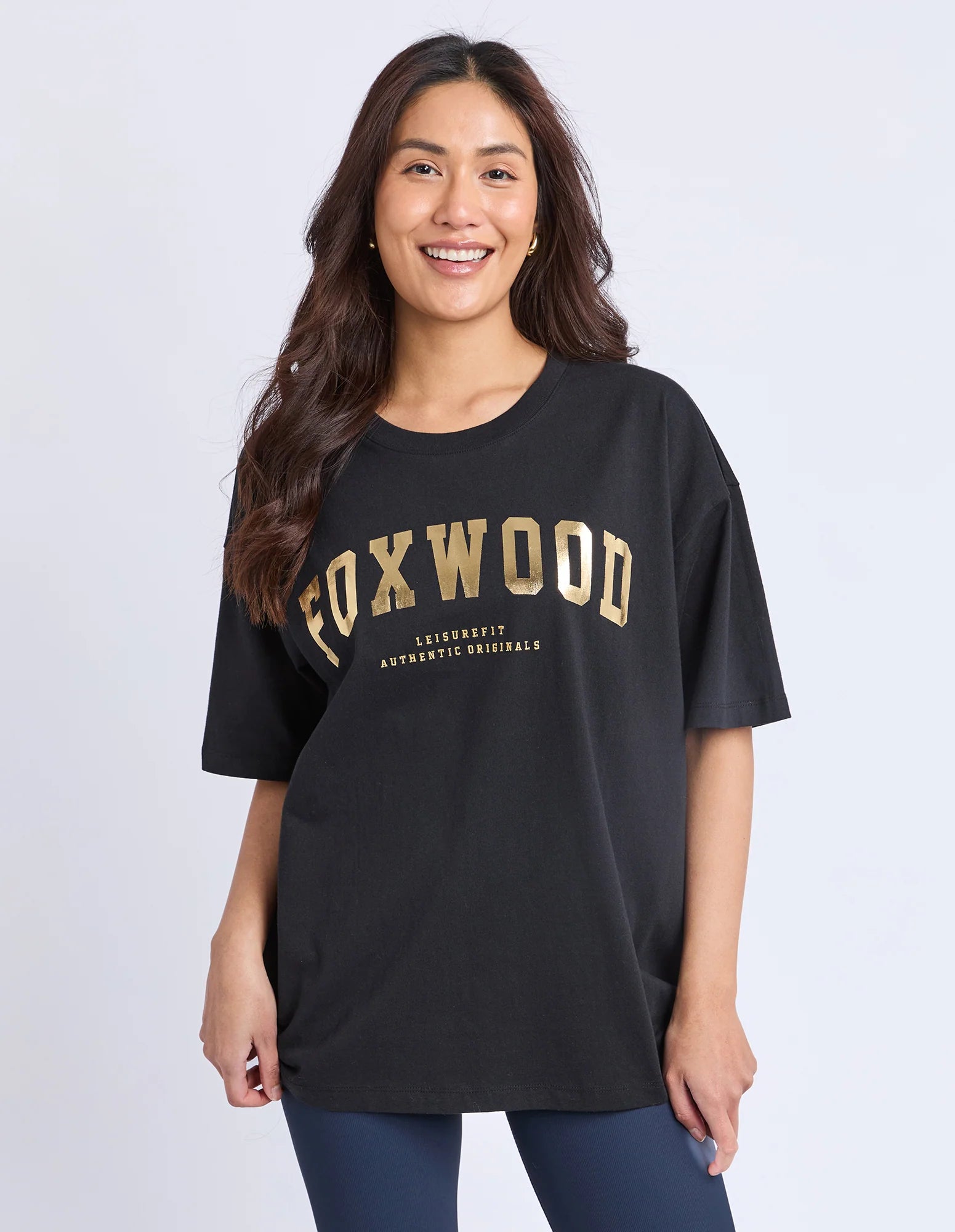 Image of Woman wearing a black t-shirt with 'FOXWOOD' printed in gold on a white background