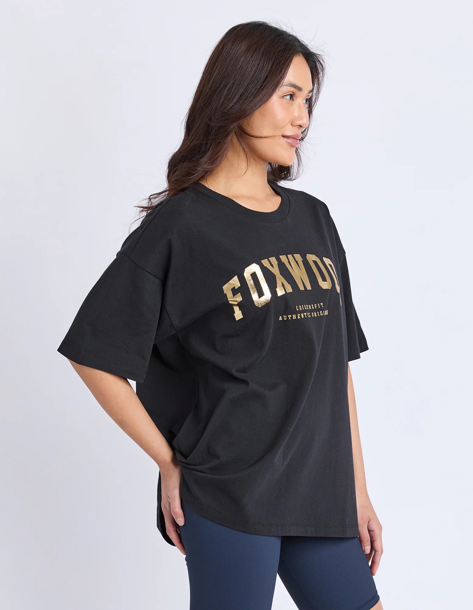 Image of Woman wearing a black t-shirt with 'FOXWOOD' printed in gold on a plain background
