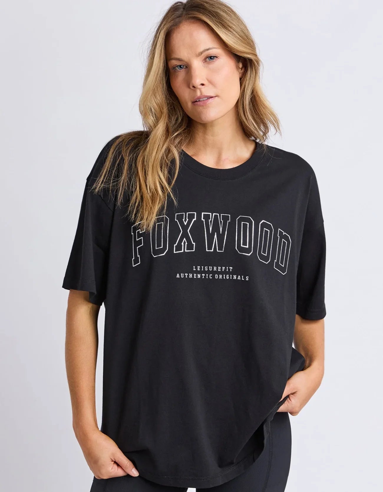 Image of Woman wearing a Foxwood black t-shirt with 'FOXWOOD' branding on a light gray background