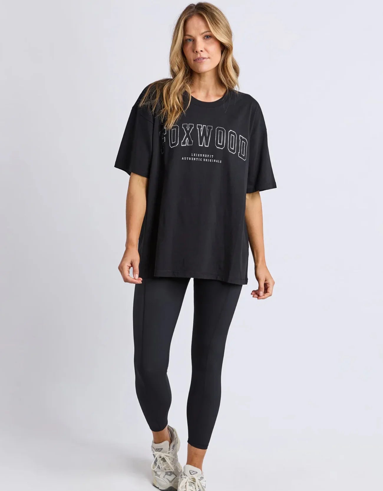 Image of Woman wearing a Foxwood black t-shirt and leggings with 'Foxwood' branding on a light gray background