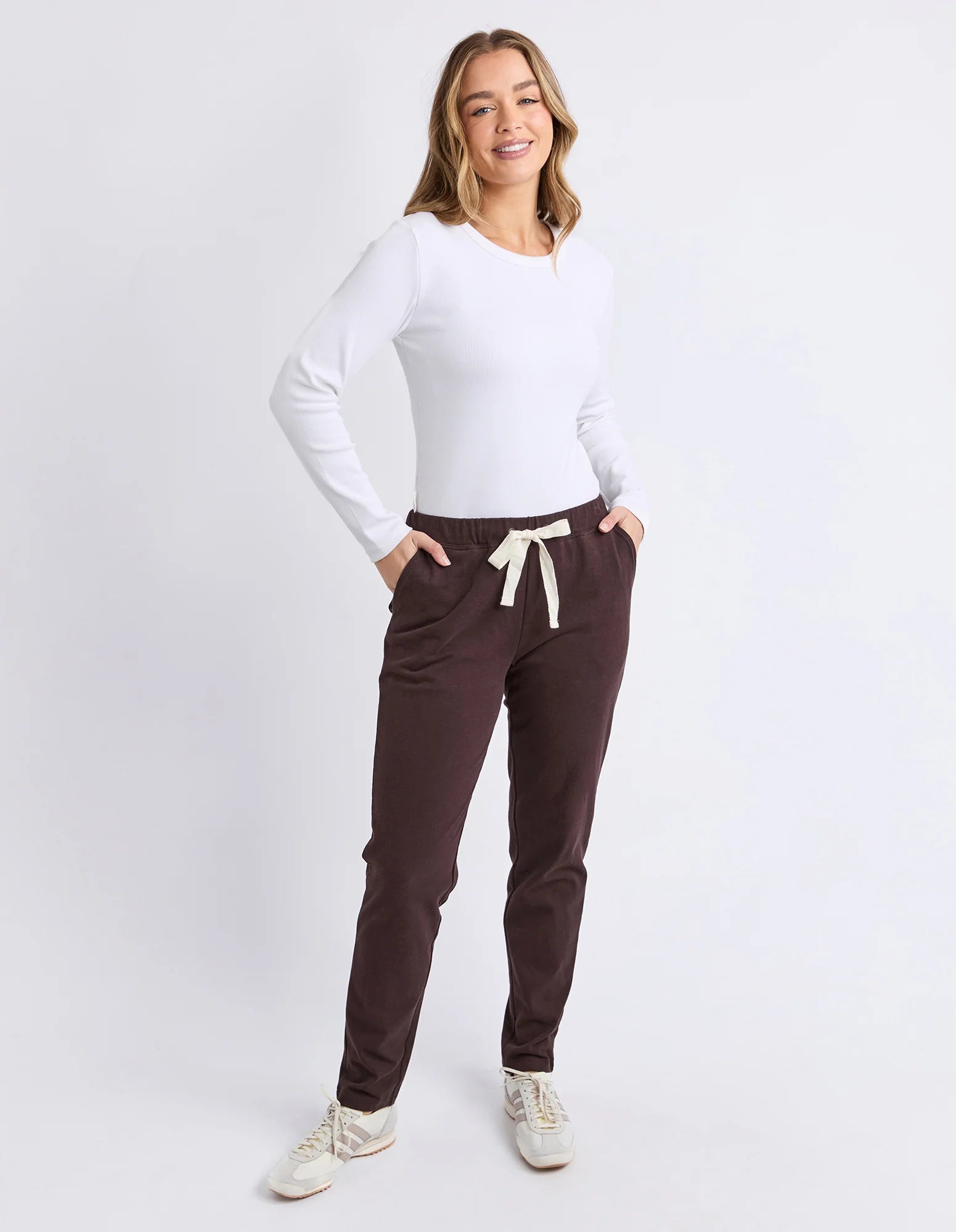 Image of Woman wearing a white long-sleeve top and Foxwood brown pants with a white background