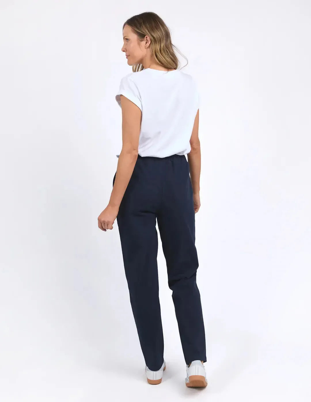 Image of Woman wearing navy trackpants paired with a white top on a plain background