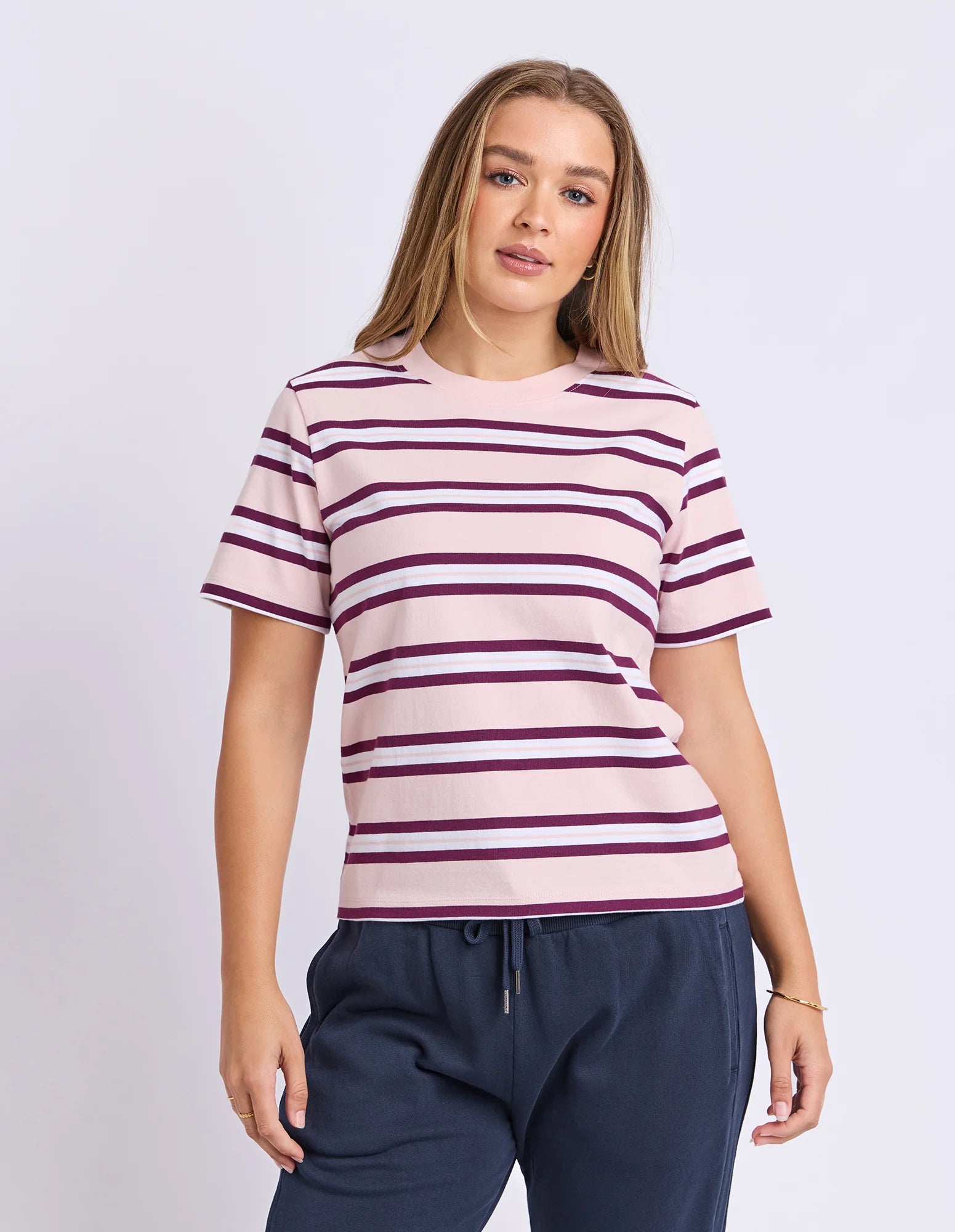 Image of Woman wearing a Foxwood pink and purple striped shirt with navy pants on a light gray background