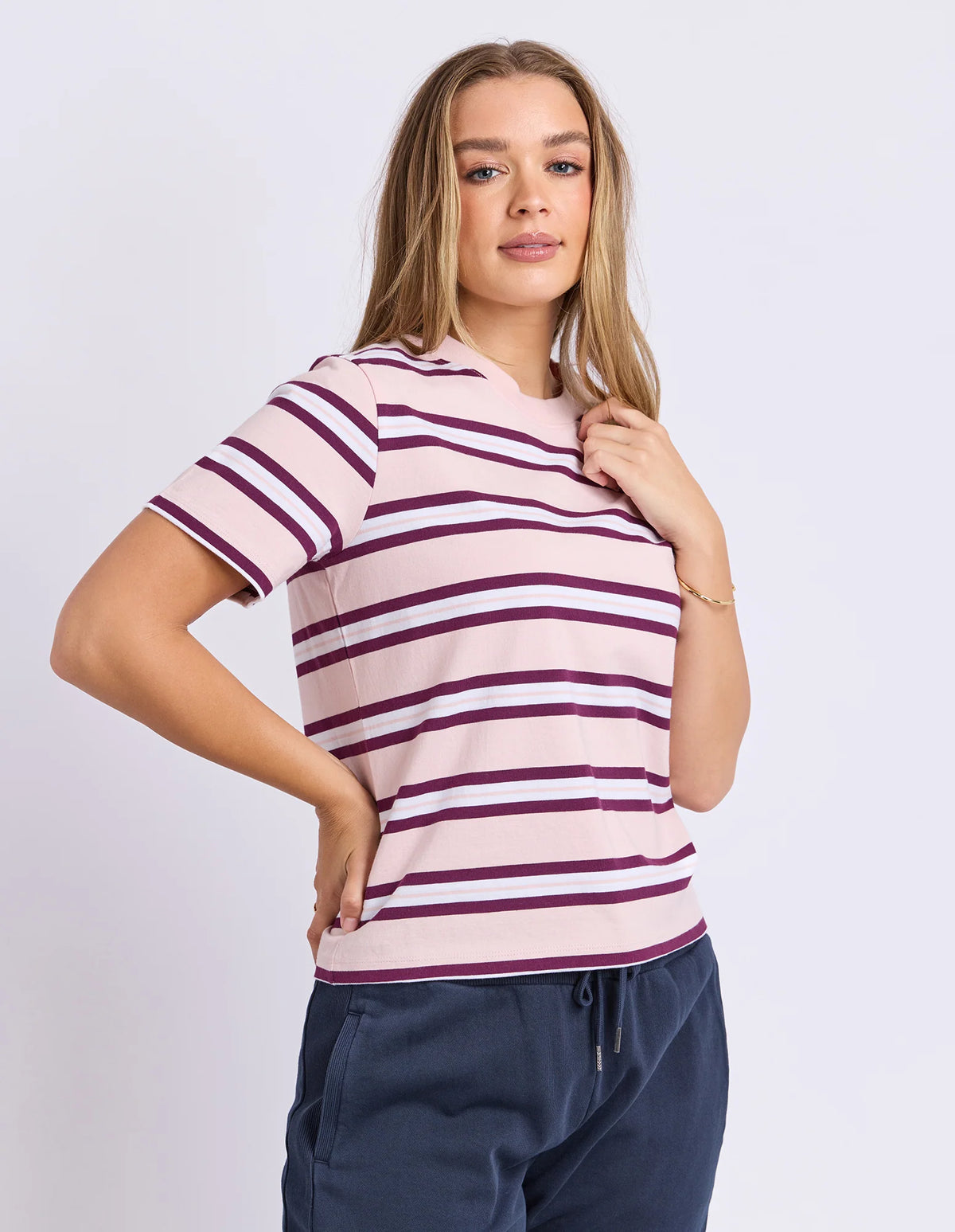 Woman wearing a Foxwood pink and purple striped shirt with navy pants on a white background