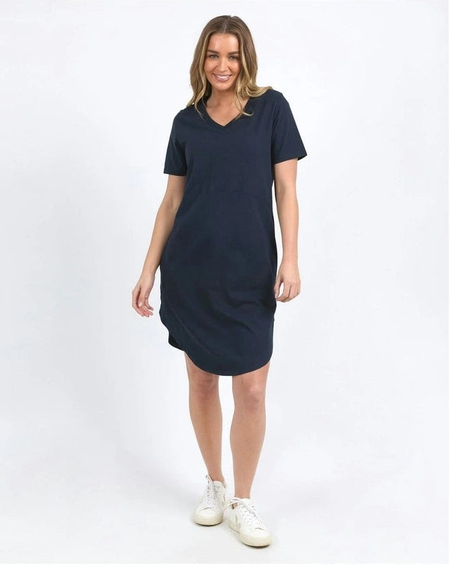 Image of A woman modeling a Foxwood short-sleeve V-neck dress in dark navy blue, paired with white sneakers, against a plain white studio background.