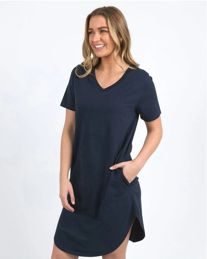 Image of A woman wearing a Foxwood navy blue short-sleeve V-neck mini dress with side pockets, standing against a light gray studio background.