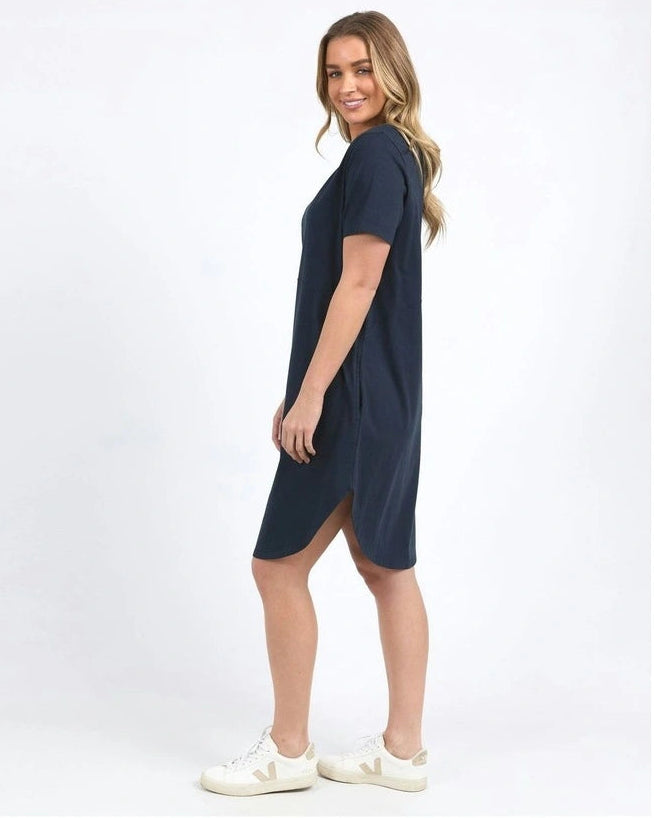 Image of A woman modeling a Foxwood short-sleeve navy blue shift dress with a side slit, paired with white sneakers, against a plain white studio background.