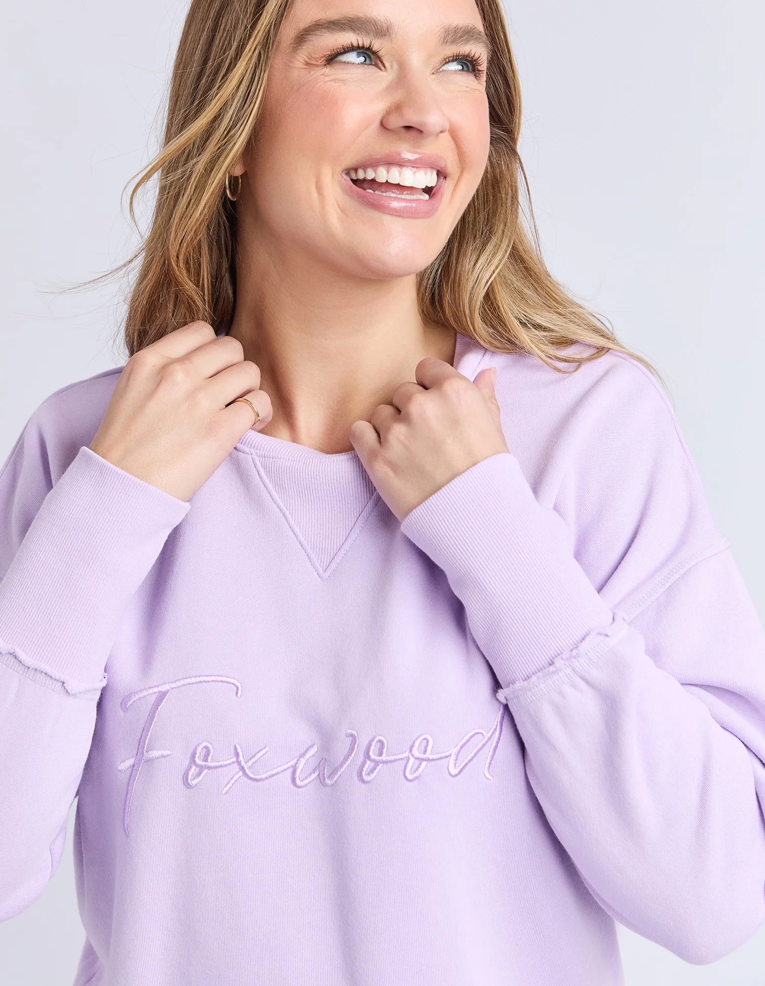 Woman wearing a Foxwood lavender sweatshirt with 'Foxwood' text on a light gray background