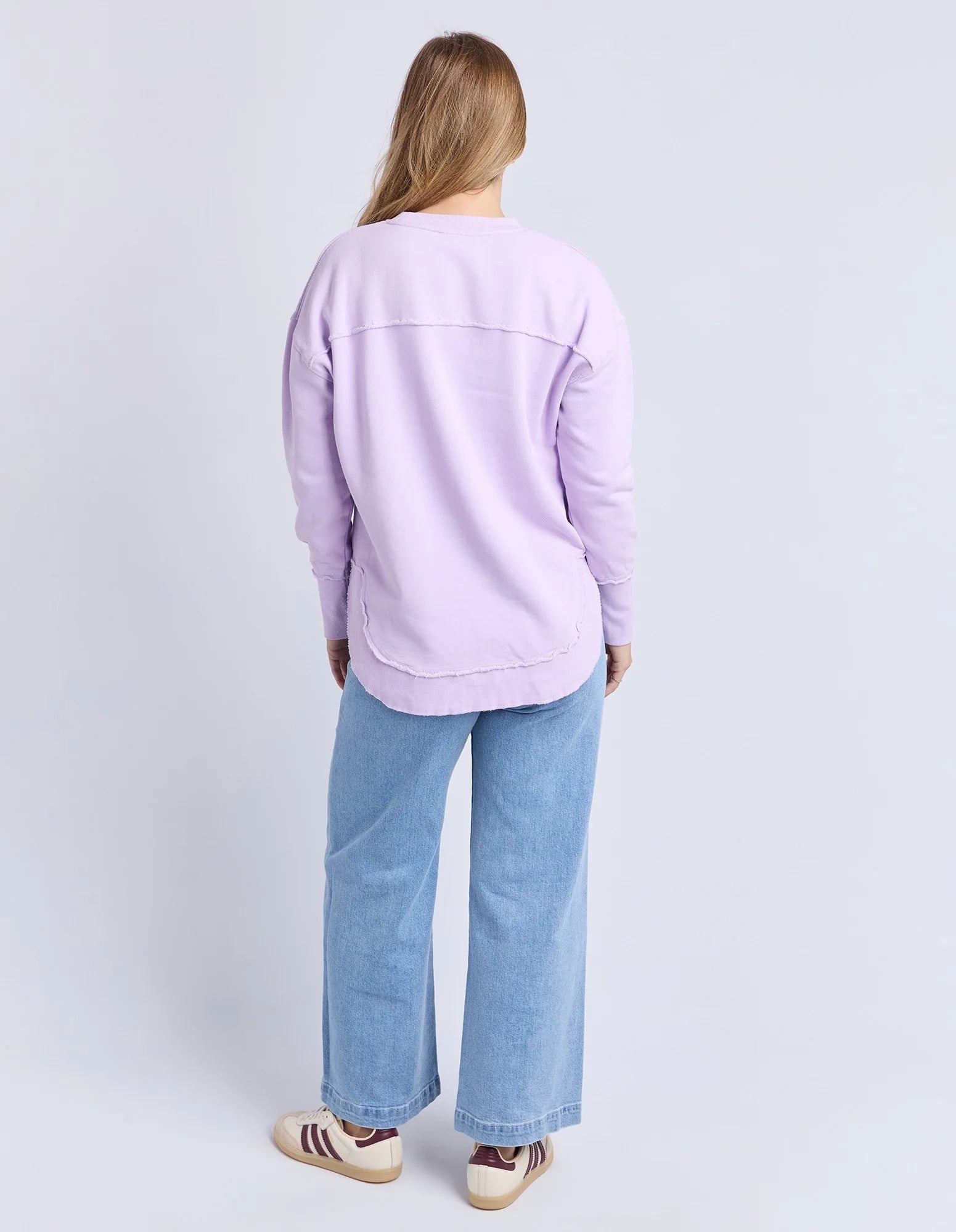 Woman wearing a Foxwood light purple sweatshirt and blue jeans on a white background
