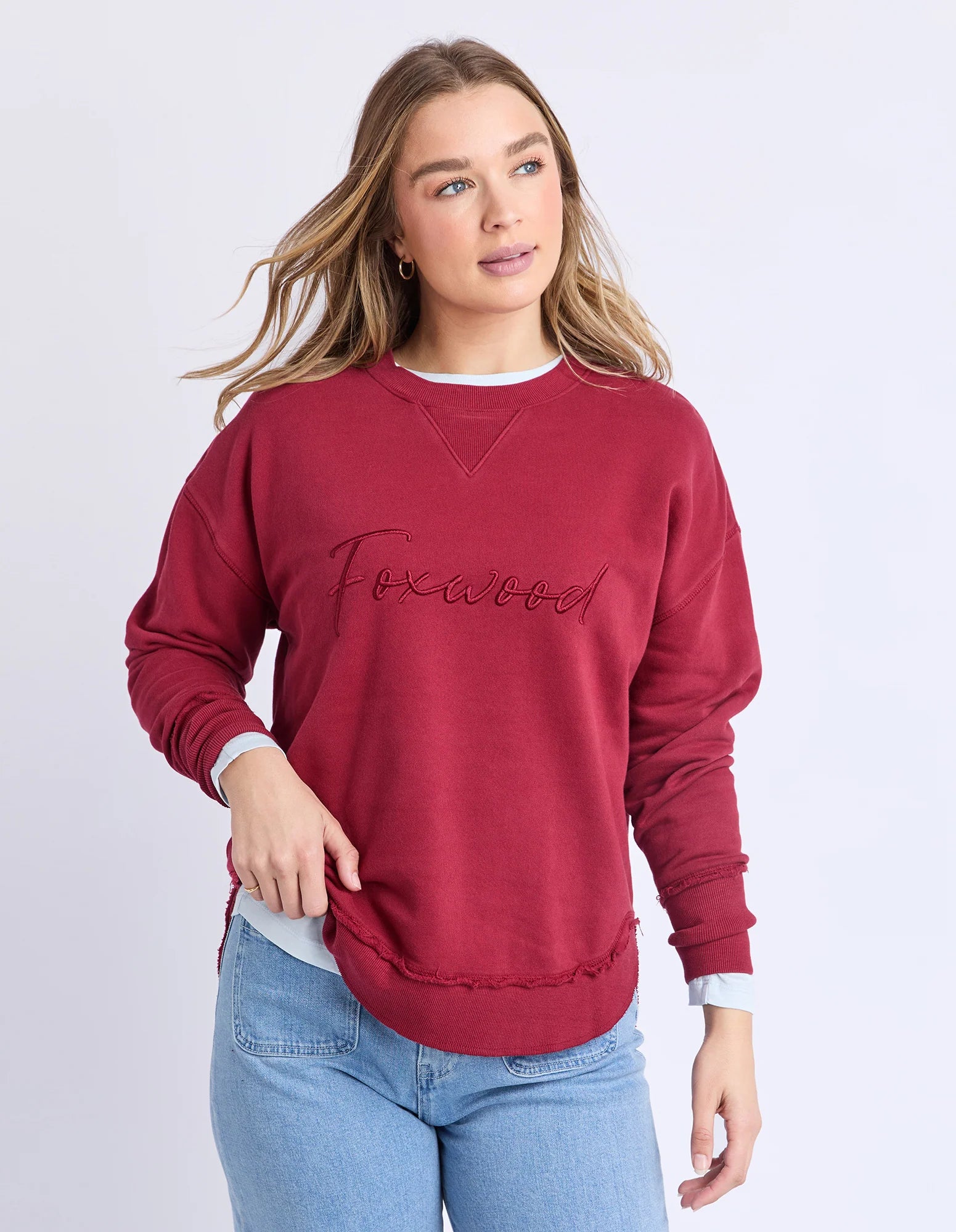 Image of Woman wearing Foxwood signature crew in rhubarb paired with denim jeans on a plain background