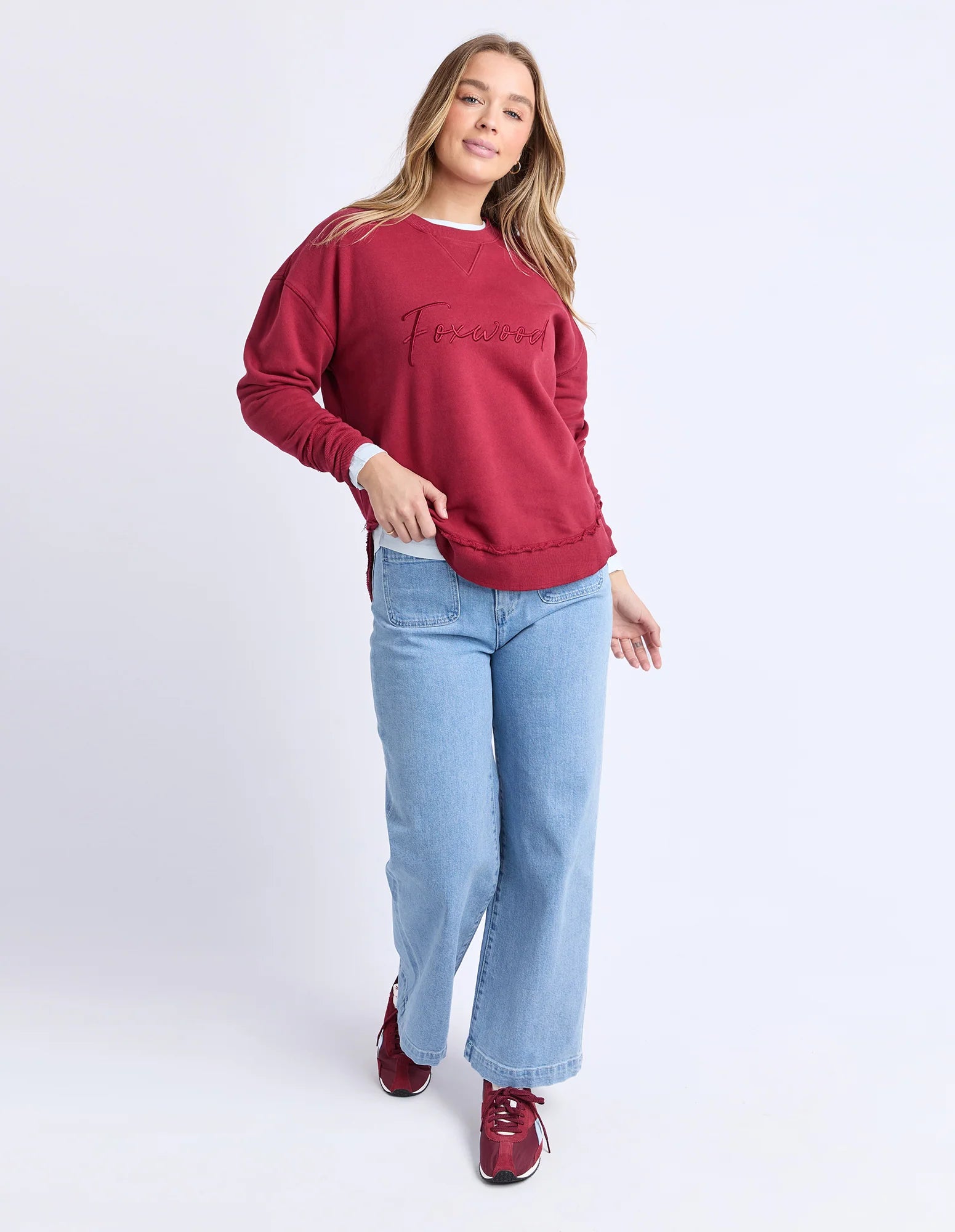 Image of Woman wearing Foxwood signature crew in rhubarb paired with denim jeans on a plain background