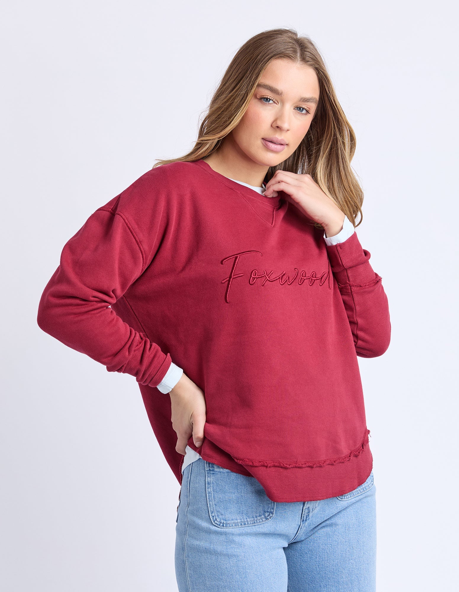 Woman wearing Foxwood signature crew in rhubarb paired with denim jeans on a plain background