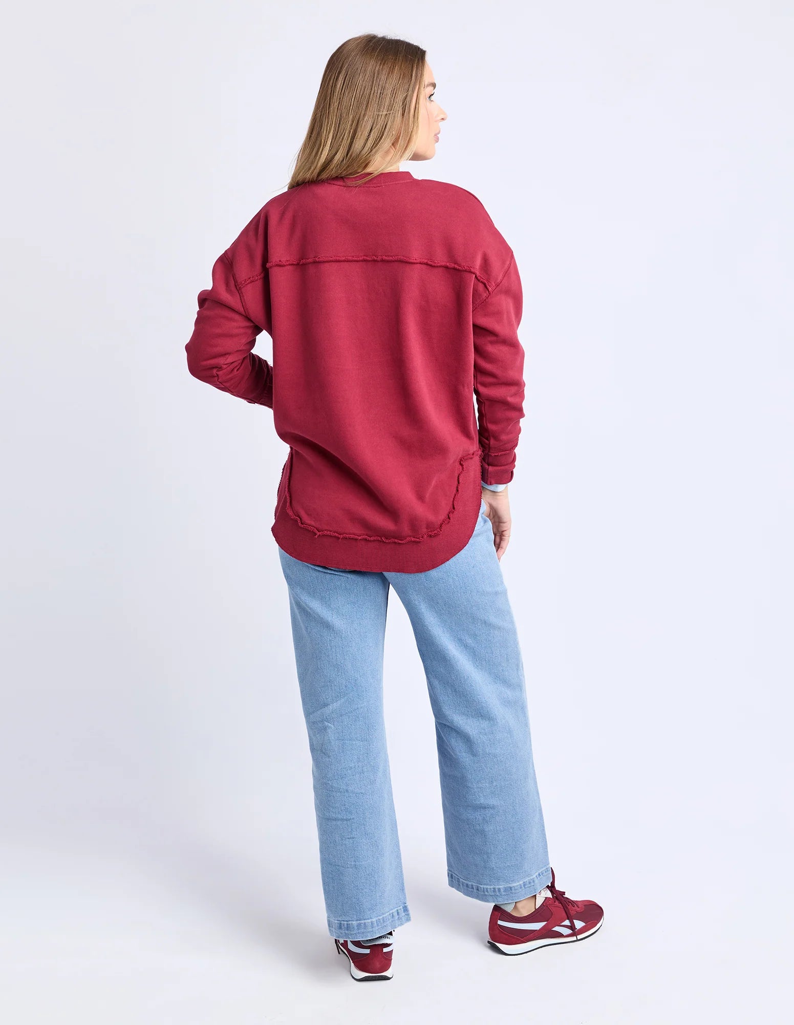 Image of Woman wearing Foxwood signature crew in rhubarb paired with denim jeans on a plain background