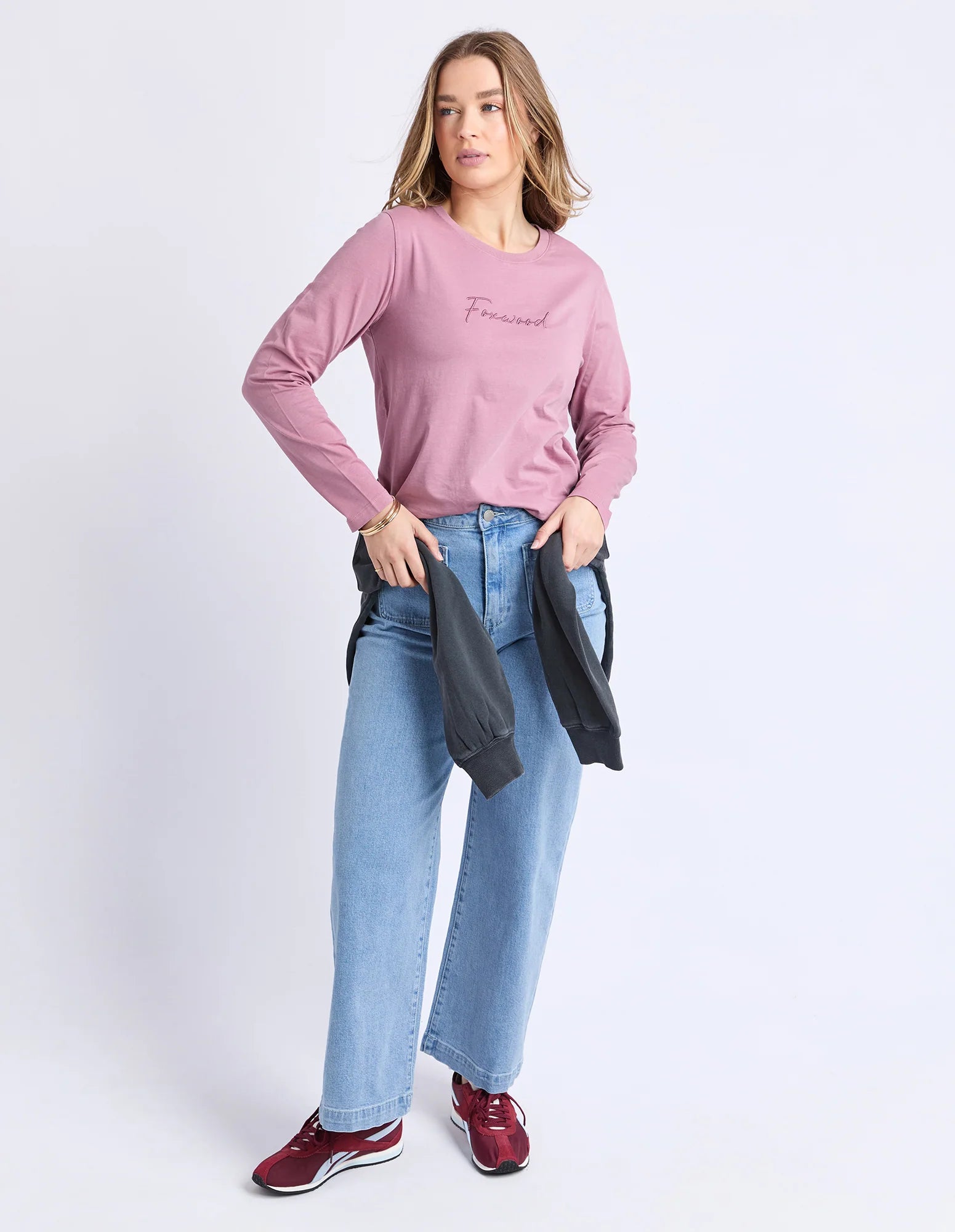 Image of Woman wearing a Foxwood pink long-sleeve shirt and blue jeans on a white background
