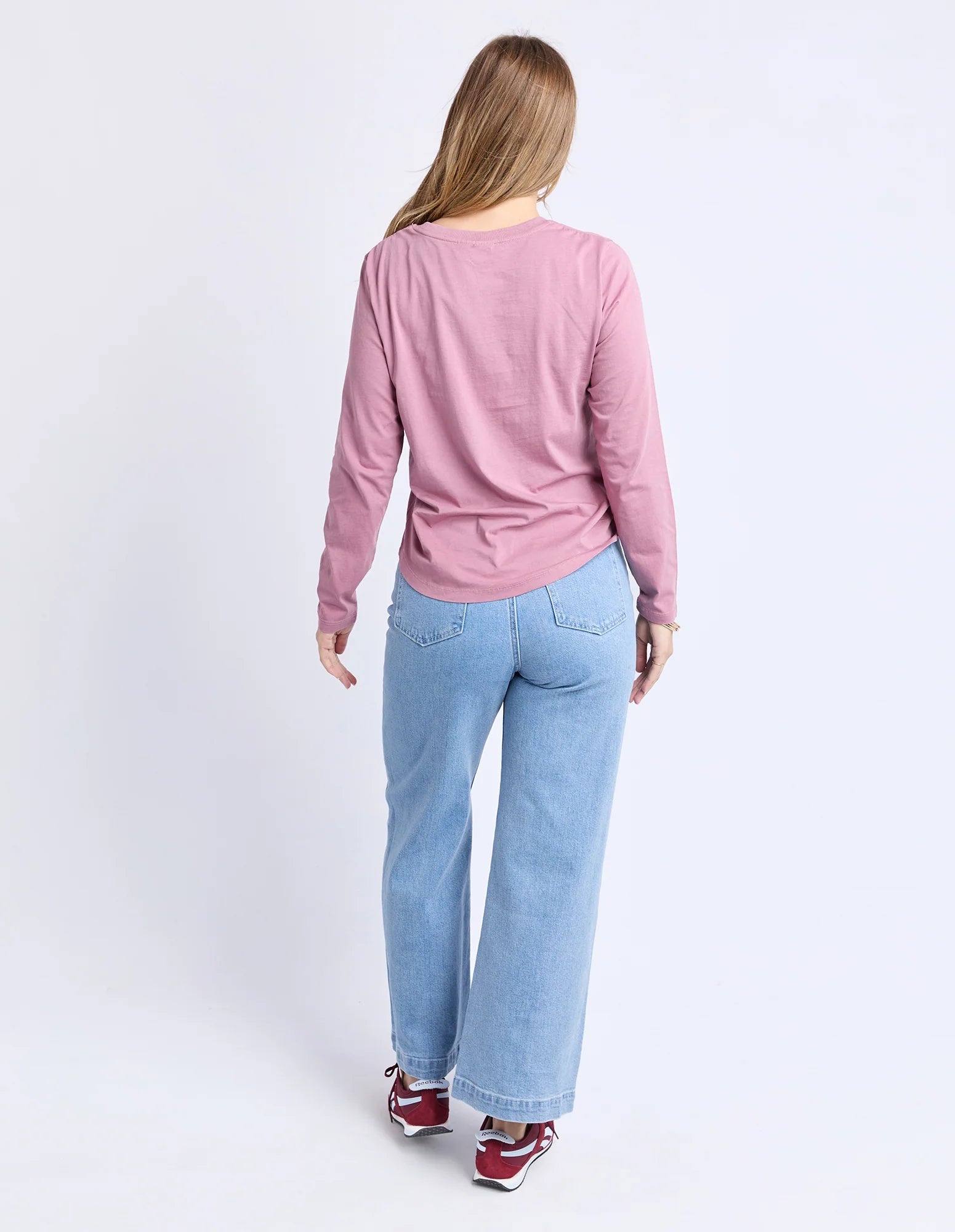 Image of Woman wearing a Foxwood pink long-sleeve shirt and light blue jeans on a white background