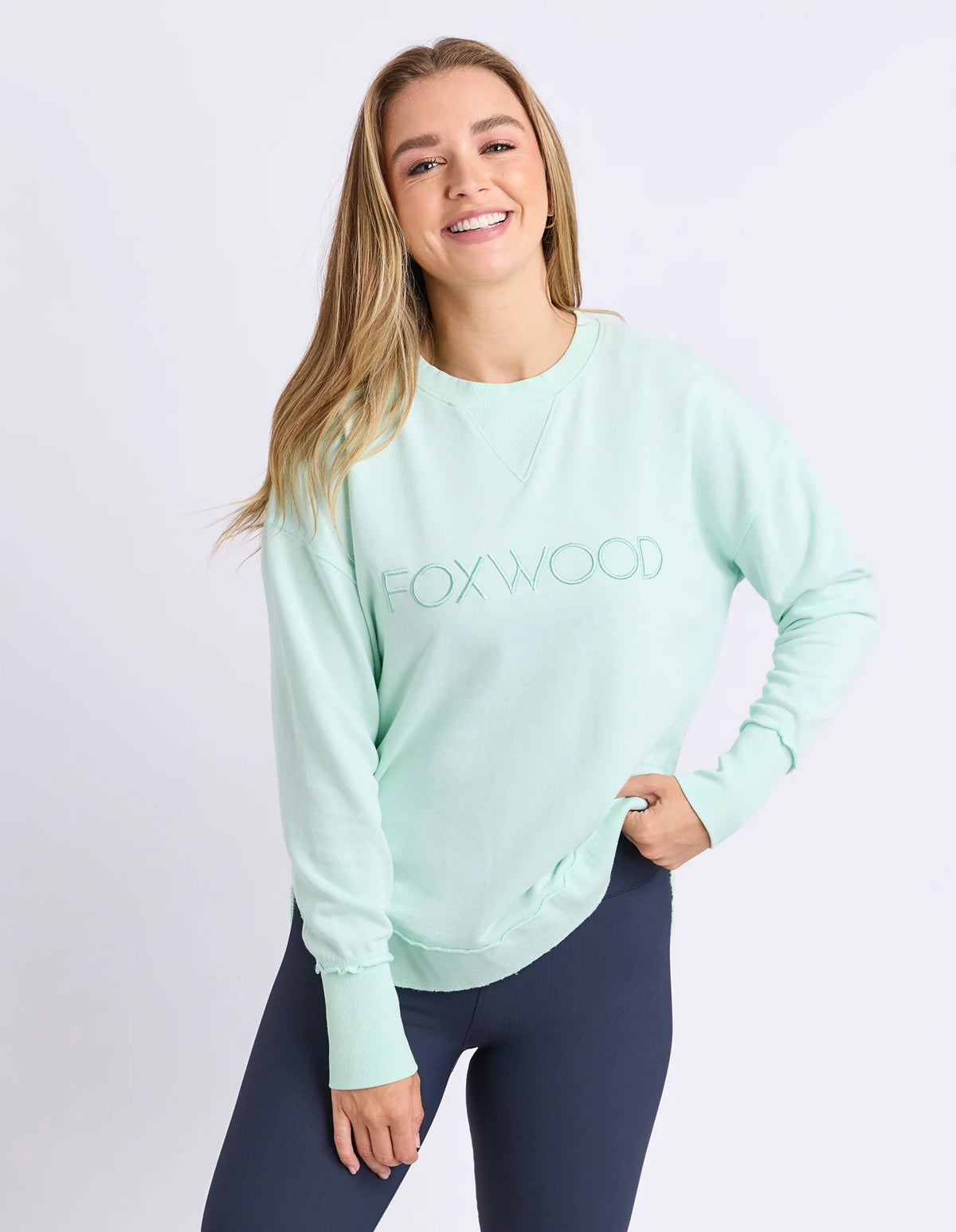 Woman wearing Foxwood simplified crew in a pale mint colour paired with navy bike shorts on a plain background