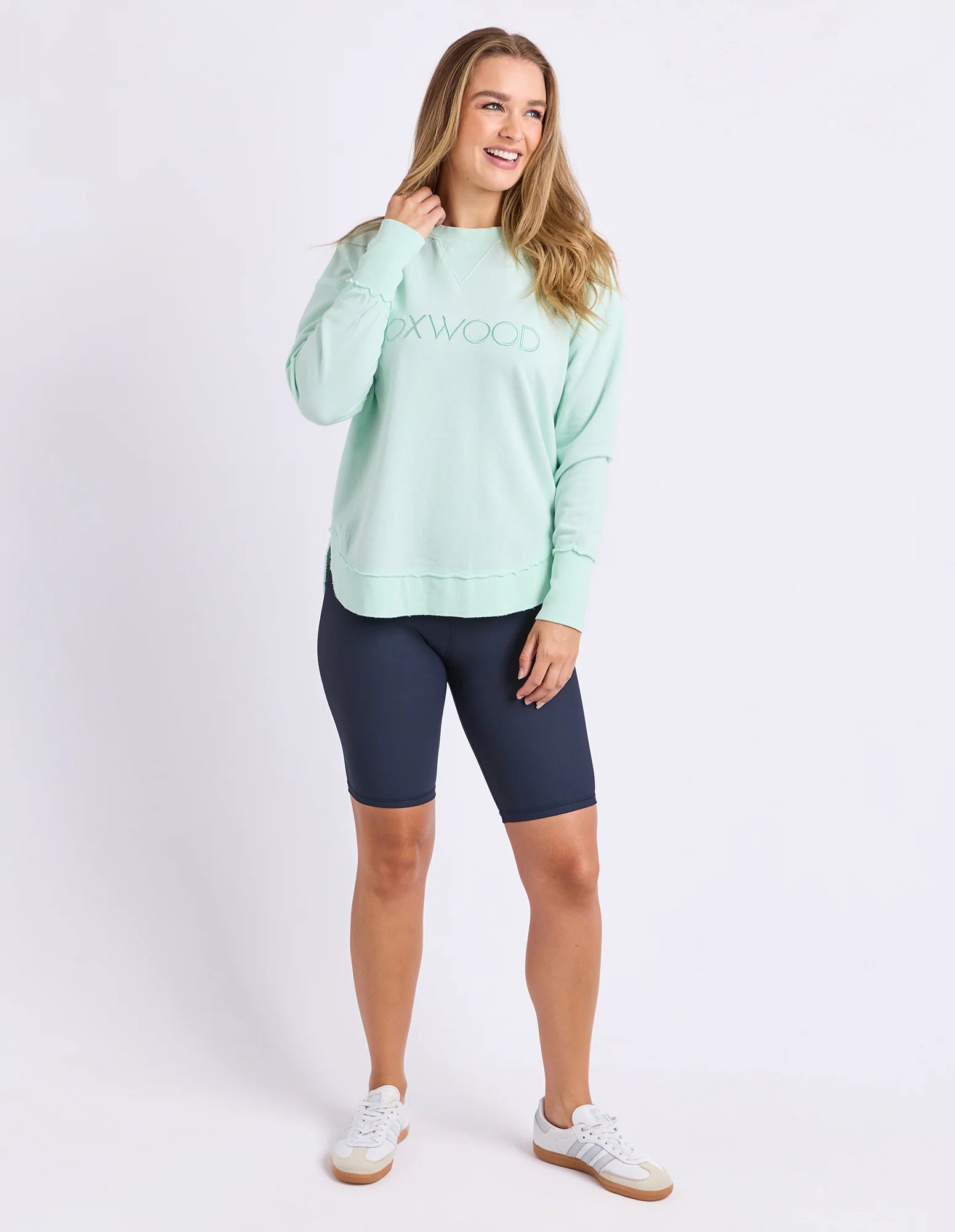 Image of Woman wearing Foxwood simplified crew in a pale mint colour paired with navy bike shorts on a plain background