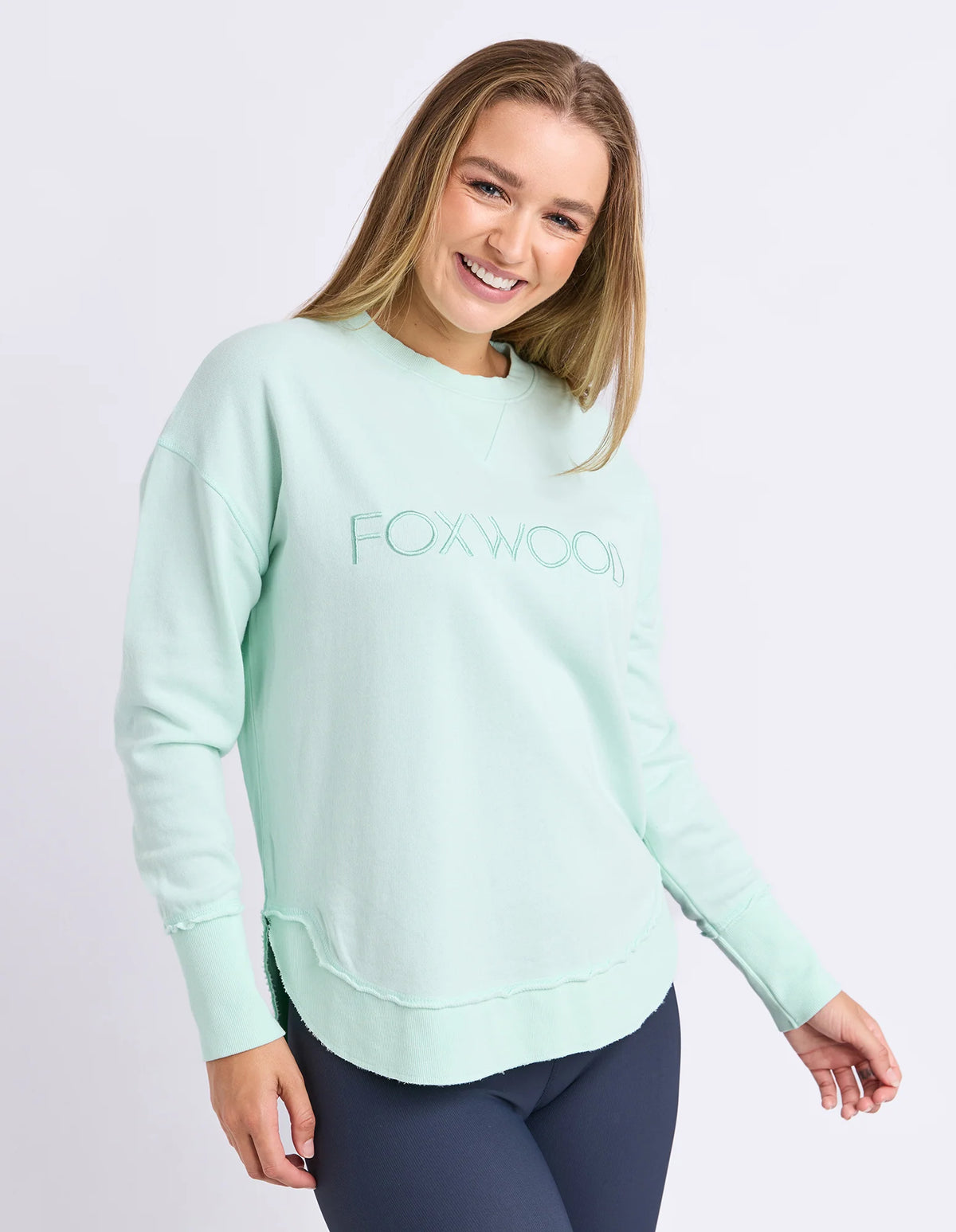 Woman wearing Foxwood simplified crew in a pale mint colour paired with navy bike shorts on a plain background