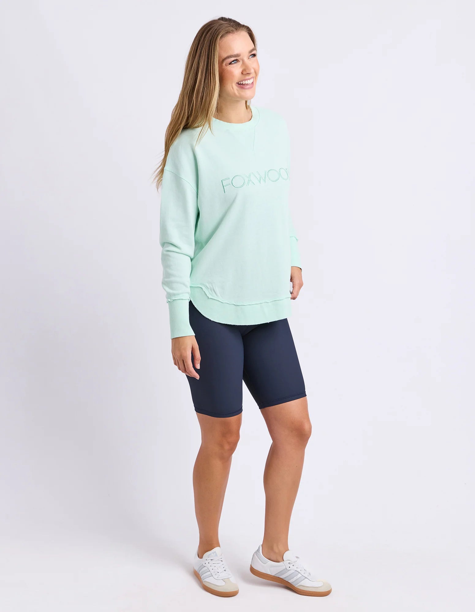 Image of Woman wearing Foxwood simplified crew in a pale mint colour paired with navy bike shorts on a plain background