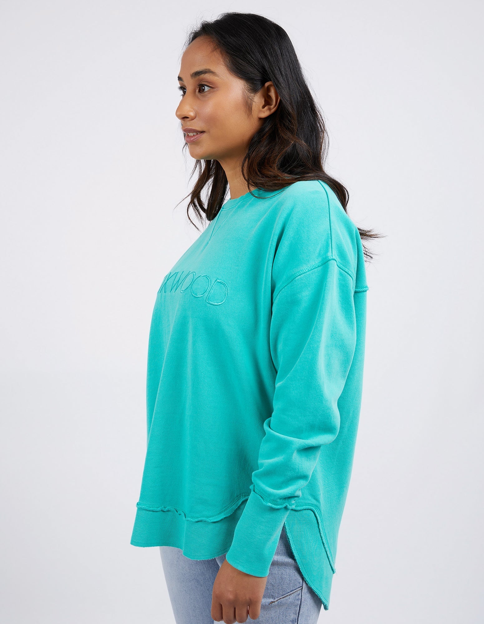 Image of Woman wearing Foxwood Simplified crew in a teal colourway paired with denim jeans on a plain background 