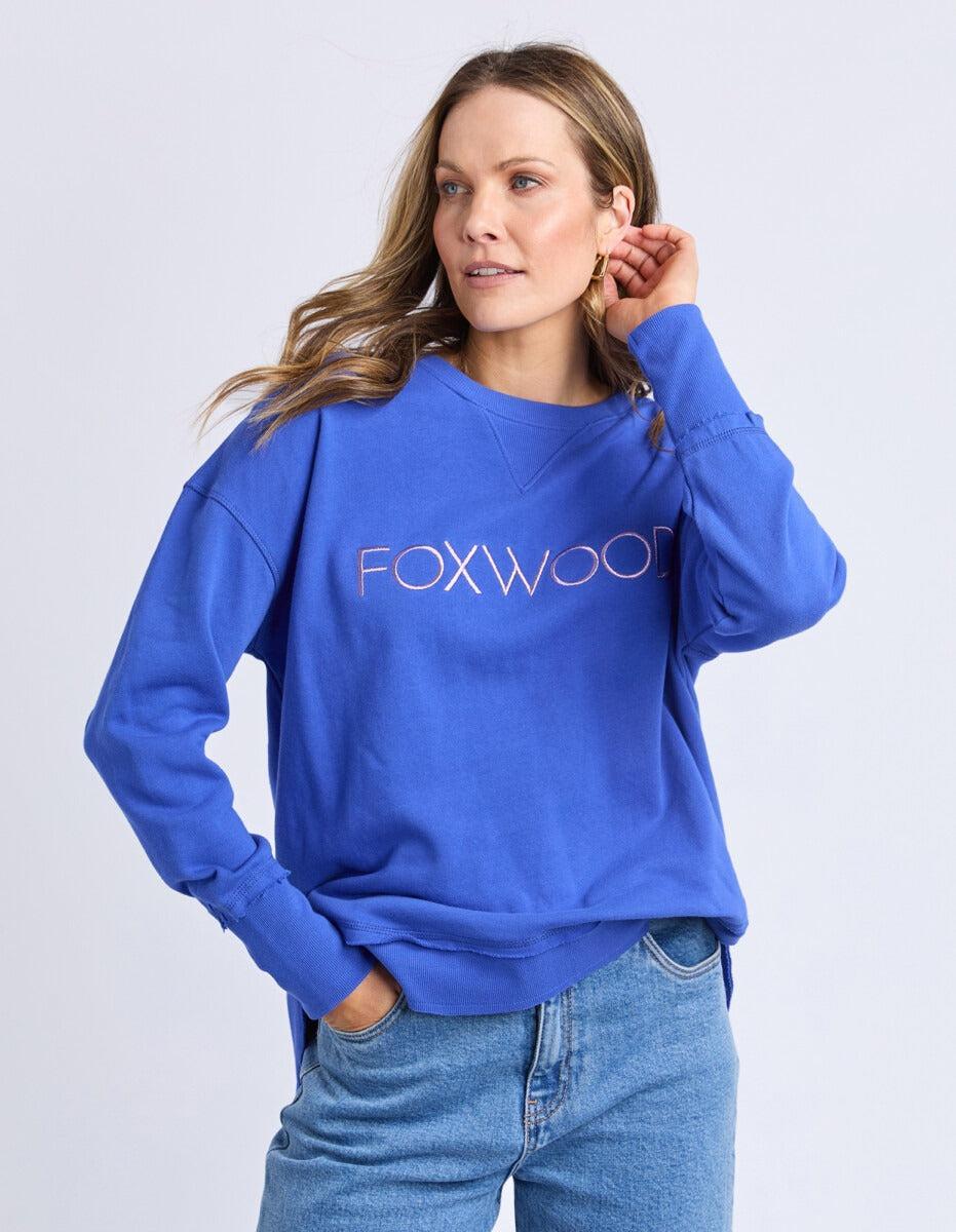 Image of Woman wearing a blue sweatshirt with 'FOXWOOD' logo on a light gray background