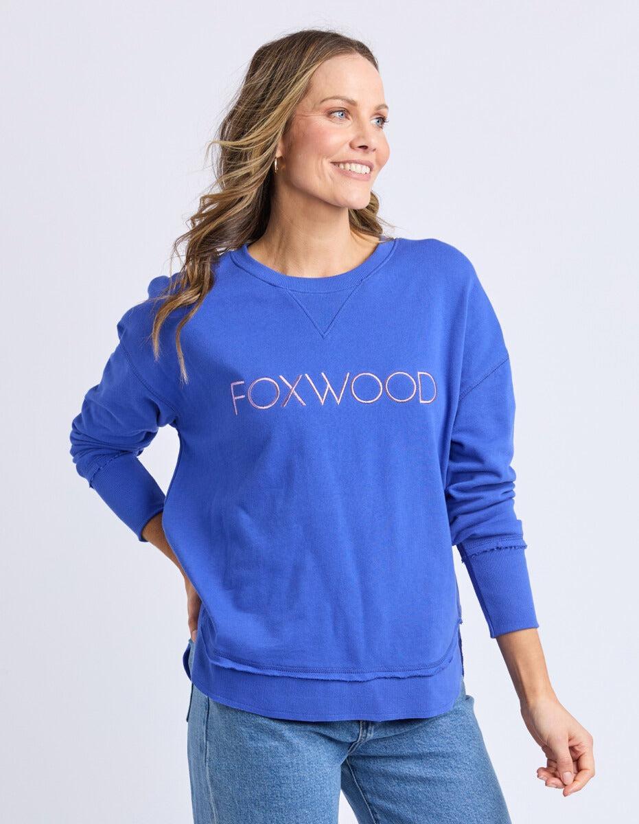 Woman wearing a blue sweatshirt with 'FOXWOOD' logo on a light gray background