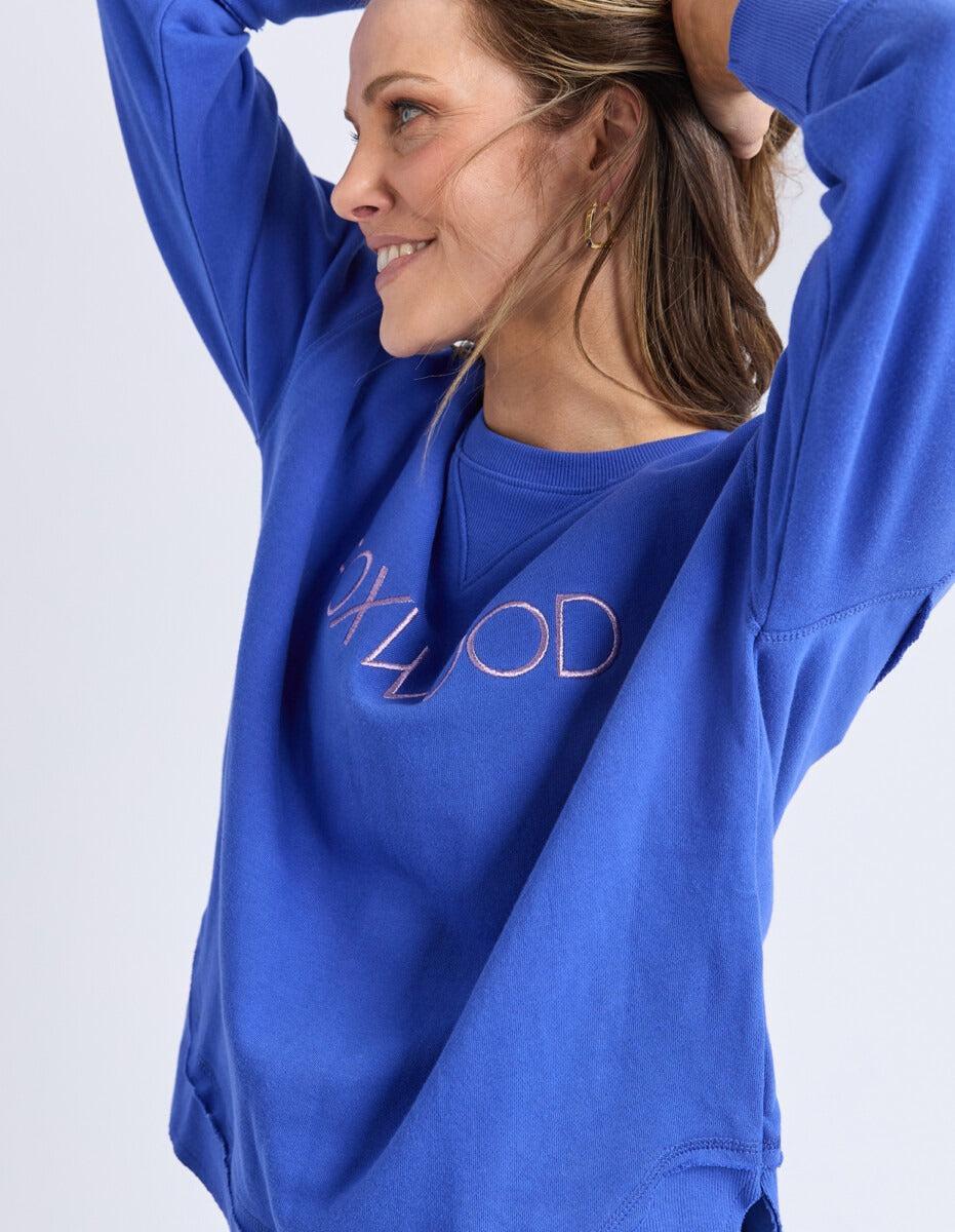 Woman wearing a Foxwood blue sweatshirt with a logo on a light gray background