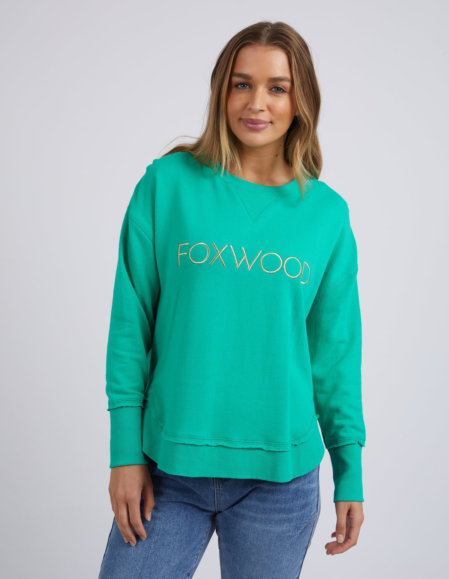 Image of Woman wearing Foxwood Simplified Metallic Crew in Bright Green paired with denim jeans on plain background 