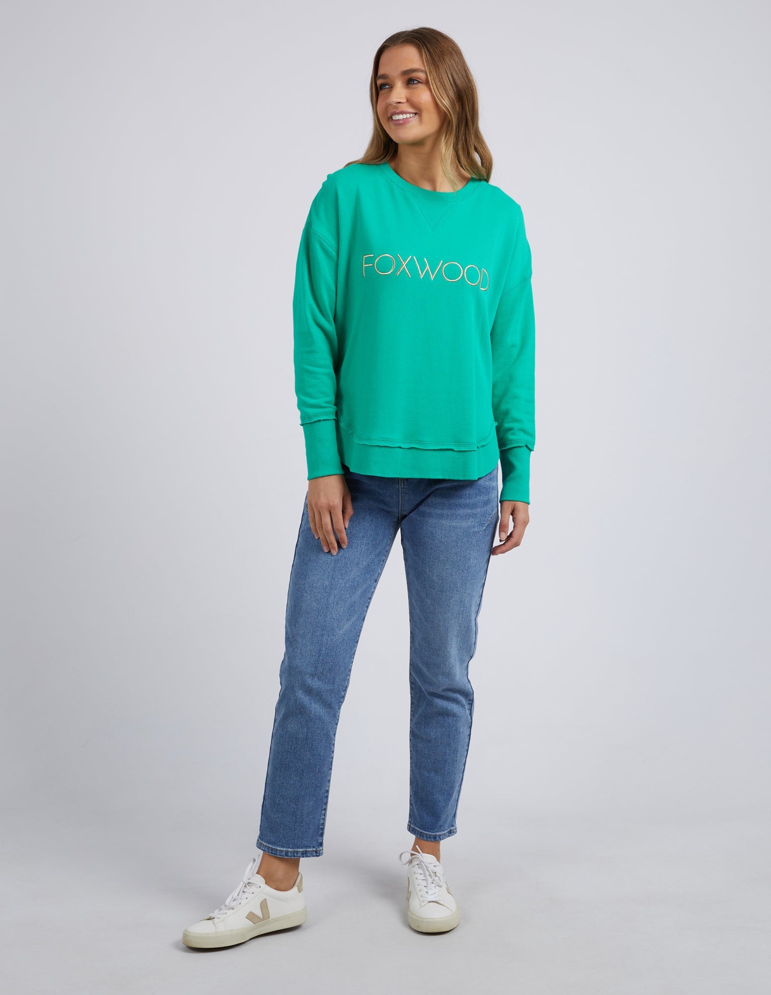 Image of Woman wearing Foxwood Simplified Metallic Crew in Bright Green paired with denim jeans on plain background 