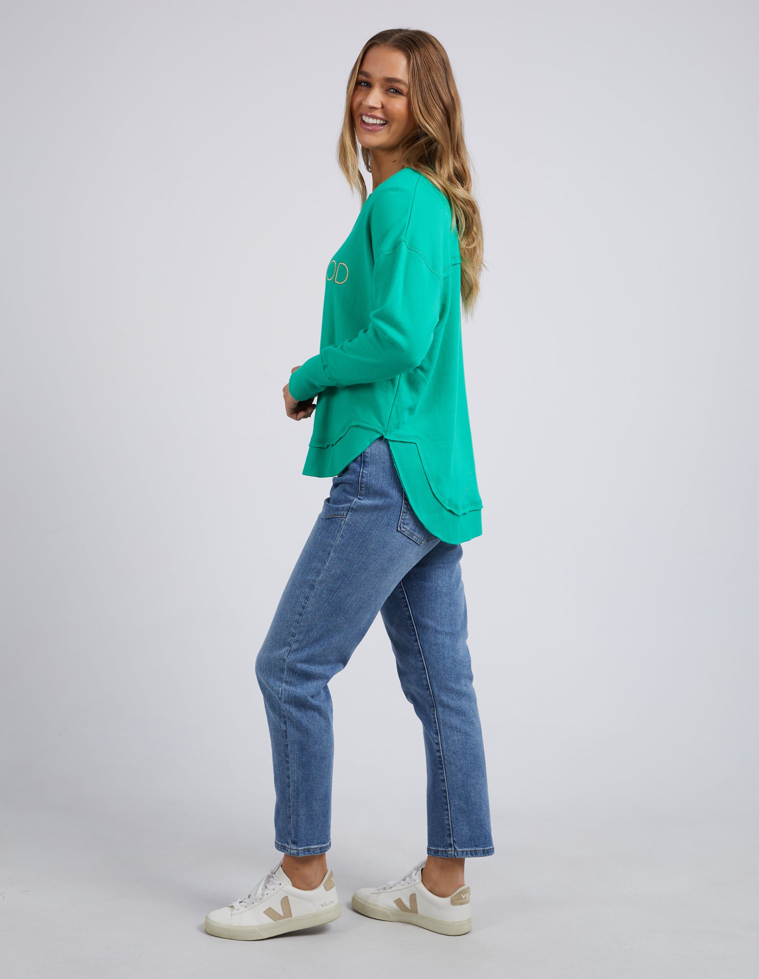 Woman wearing Foxwood Simplified Metallic Crew in Bright Green paired with denim jeans on plain background 