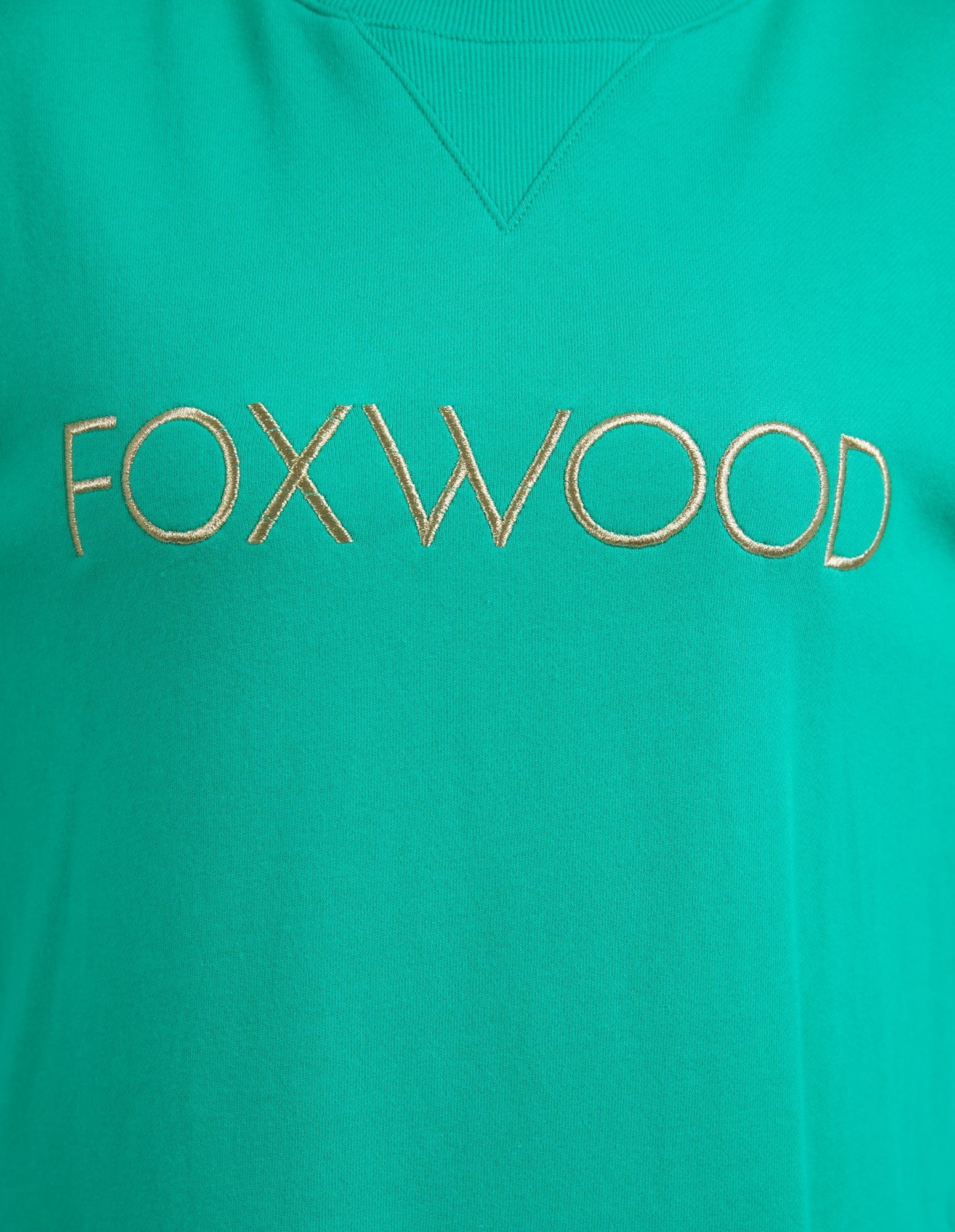 Image of Woman wearing Foxwood Simplified Metallic Crew in Bright Green paired with denim jeans on plain background 