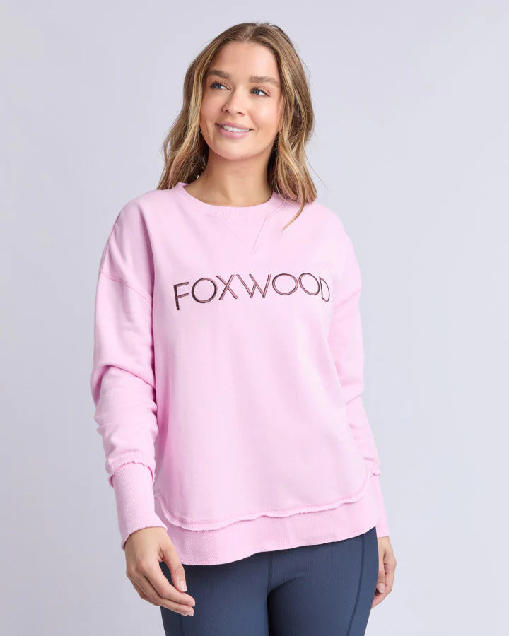 Image of Woman wearing a pink 'FOXWOOD' sweatshirt on a light gray background