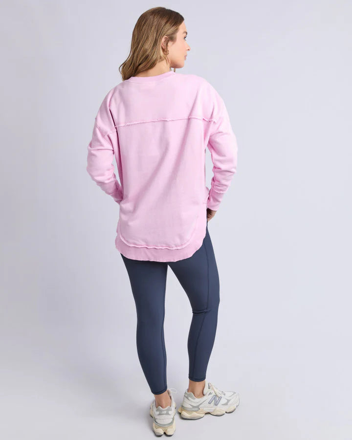 Image of Woman wearing a Foxwood pink sweatshirt and dark blue leggings on a light gray background