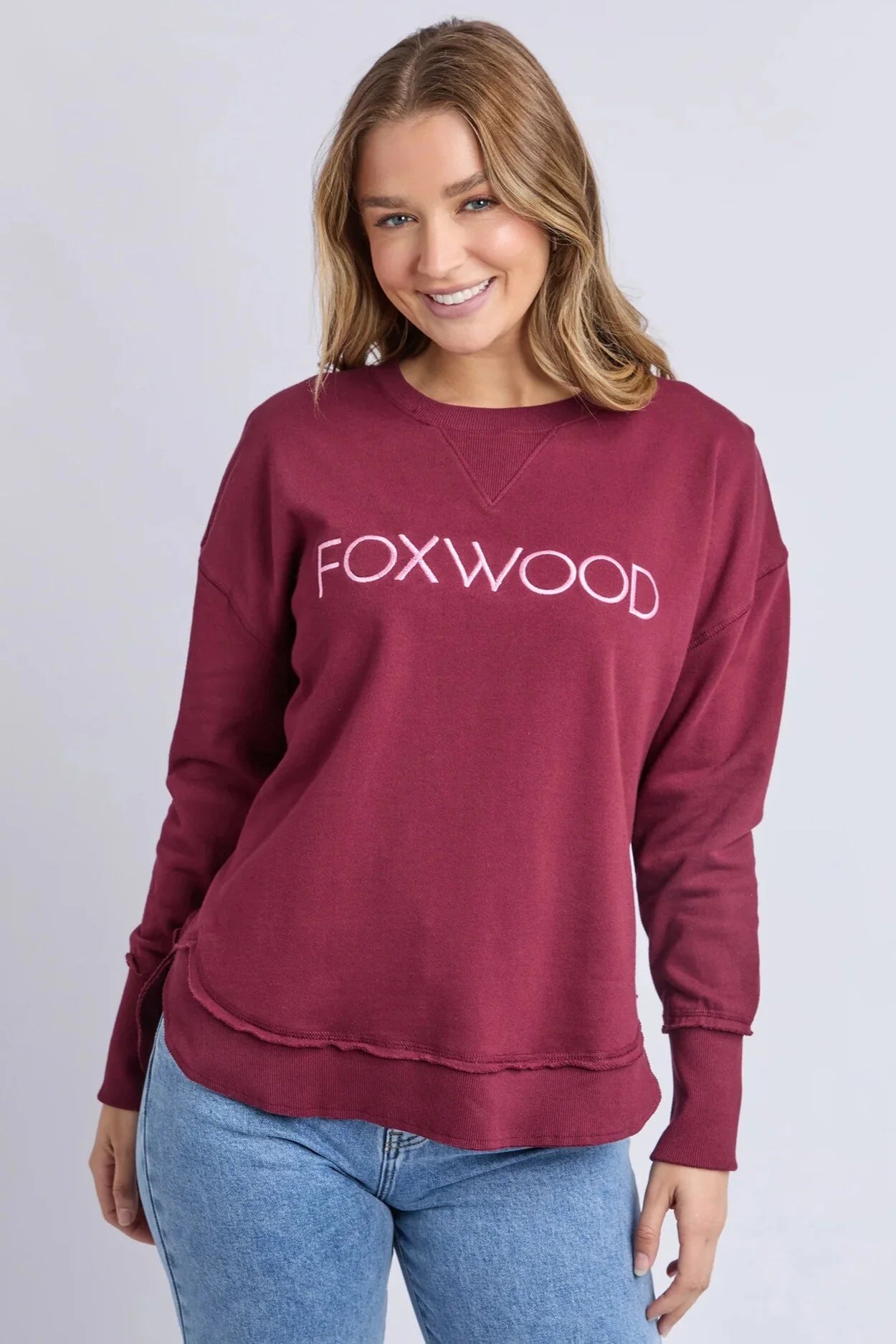 Image of Woman wearing a Foxwood Simplified Metallic crew in burgundy paired with denim jeans on a plain background