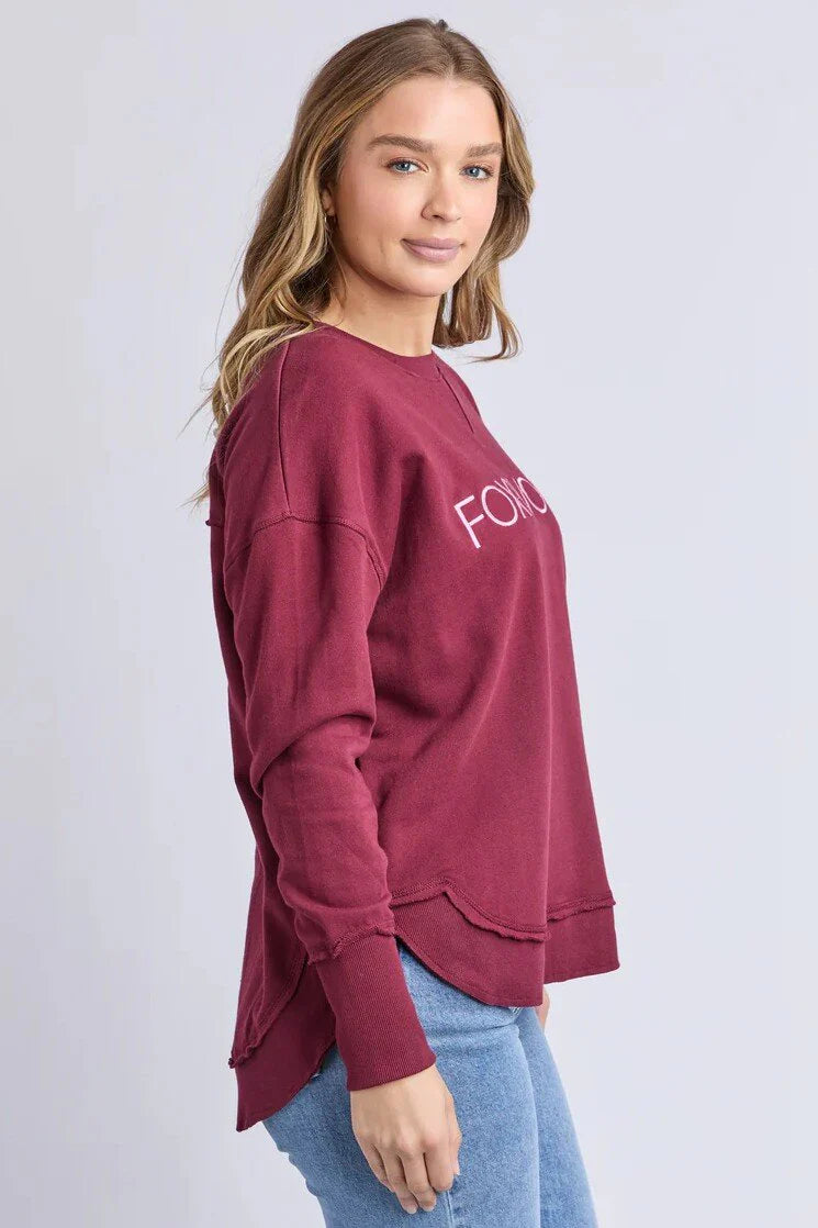 Woman wearing a Foxwood Simplified Metallic crew in burgundy paired with denim jeans on a plain background