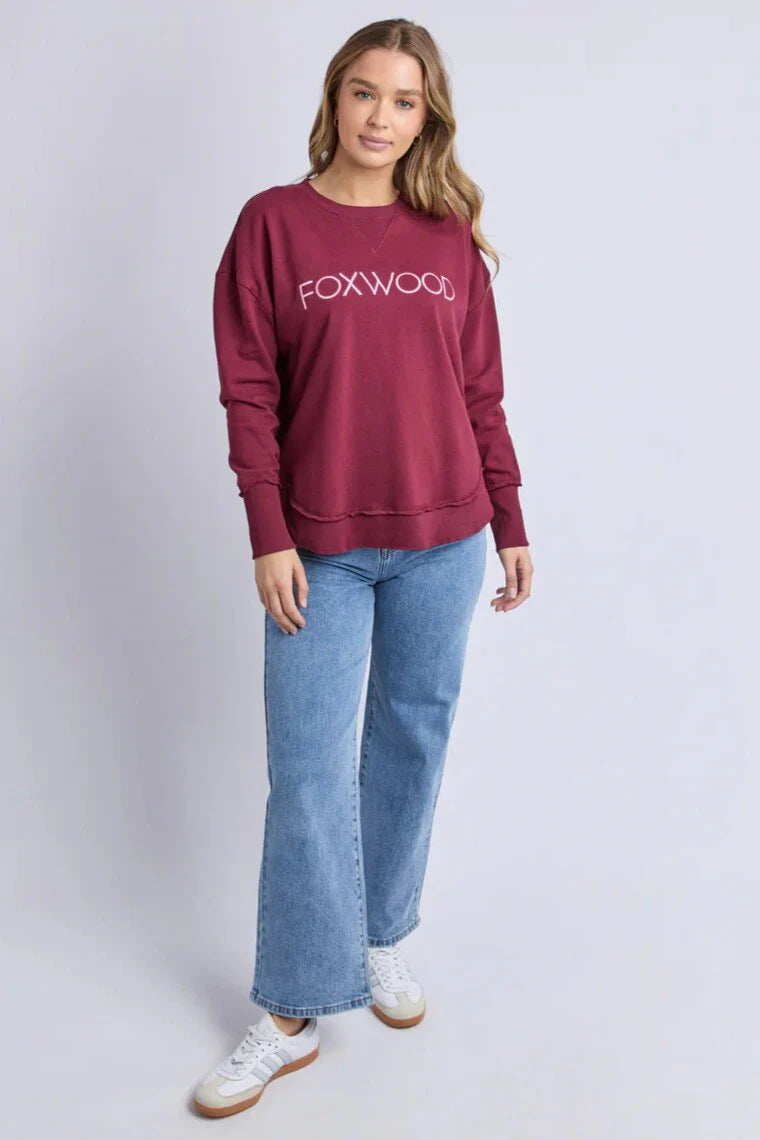 Woman wearing a Foxwood Simplified Metallic crew in burgundy paired with denim jeans on a plain background